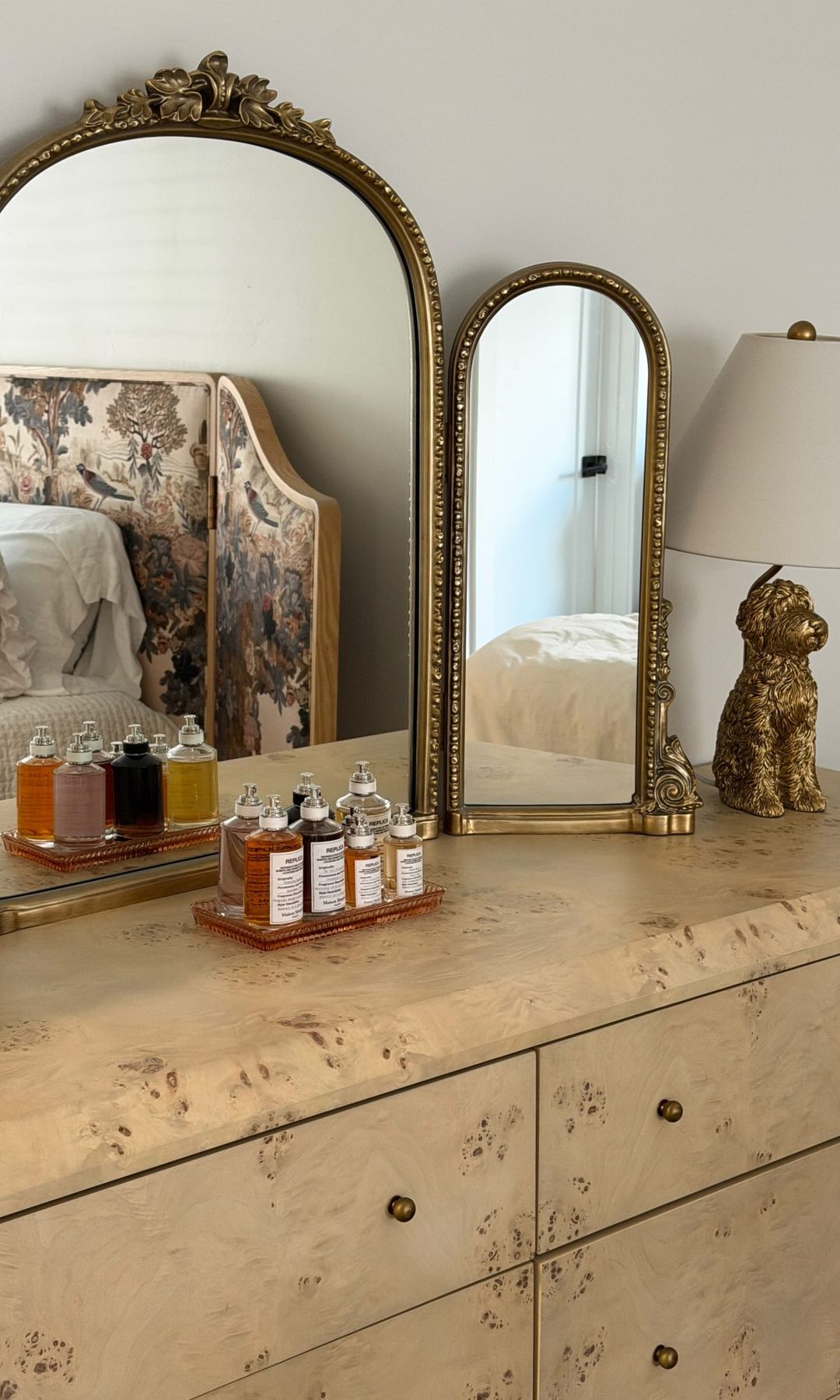 Varios frascos de perfume y cosméticos colocados sobre una cómoda frente a dos espejos