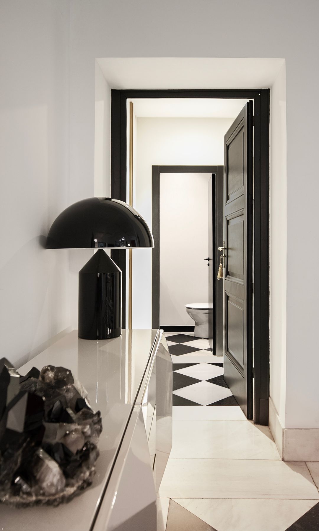Puerta negra que conduce, mediante un suelo de damero blanco y negro a un aseo de cortesía