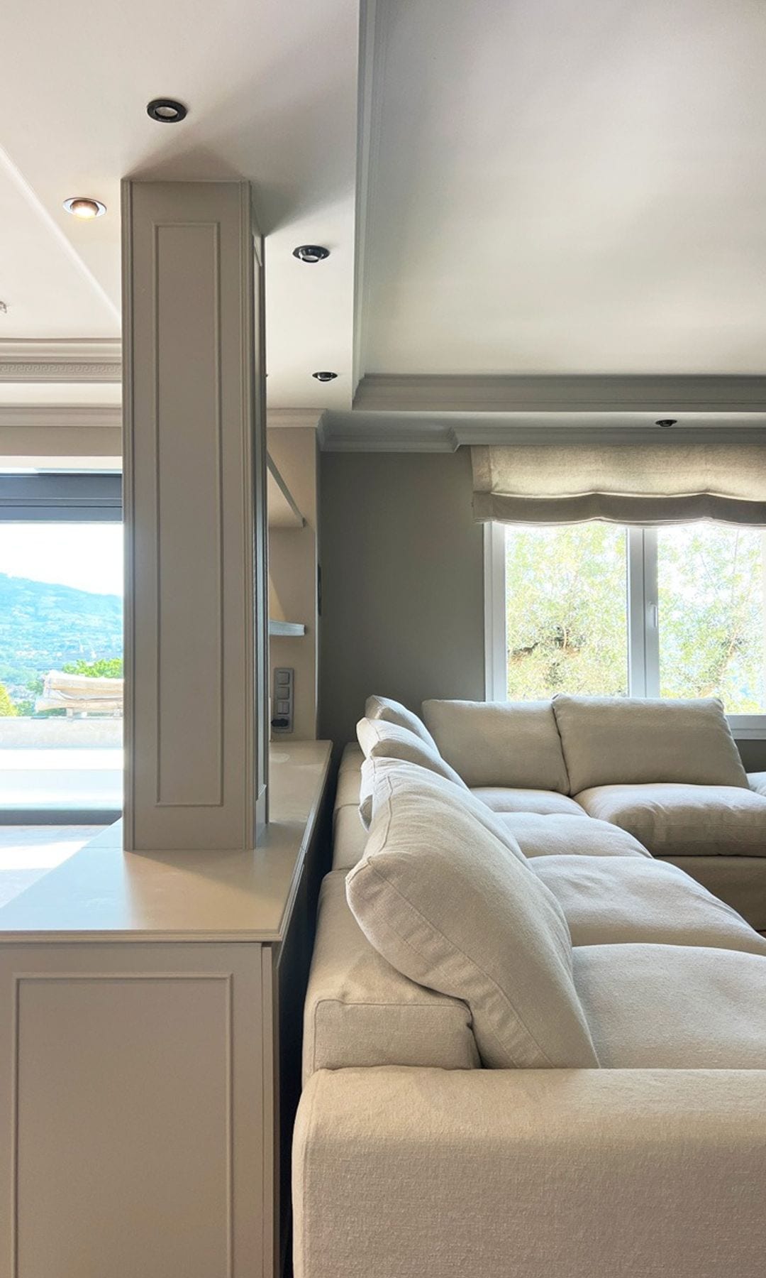 Salón con sofá blanco y estantería abierta que lo separa del comedor, ventanas con estores blancos