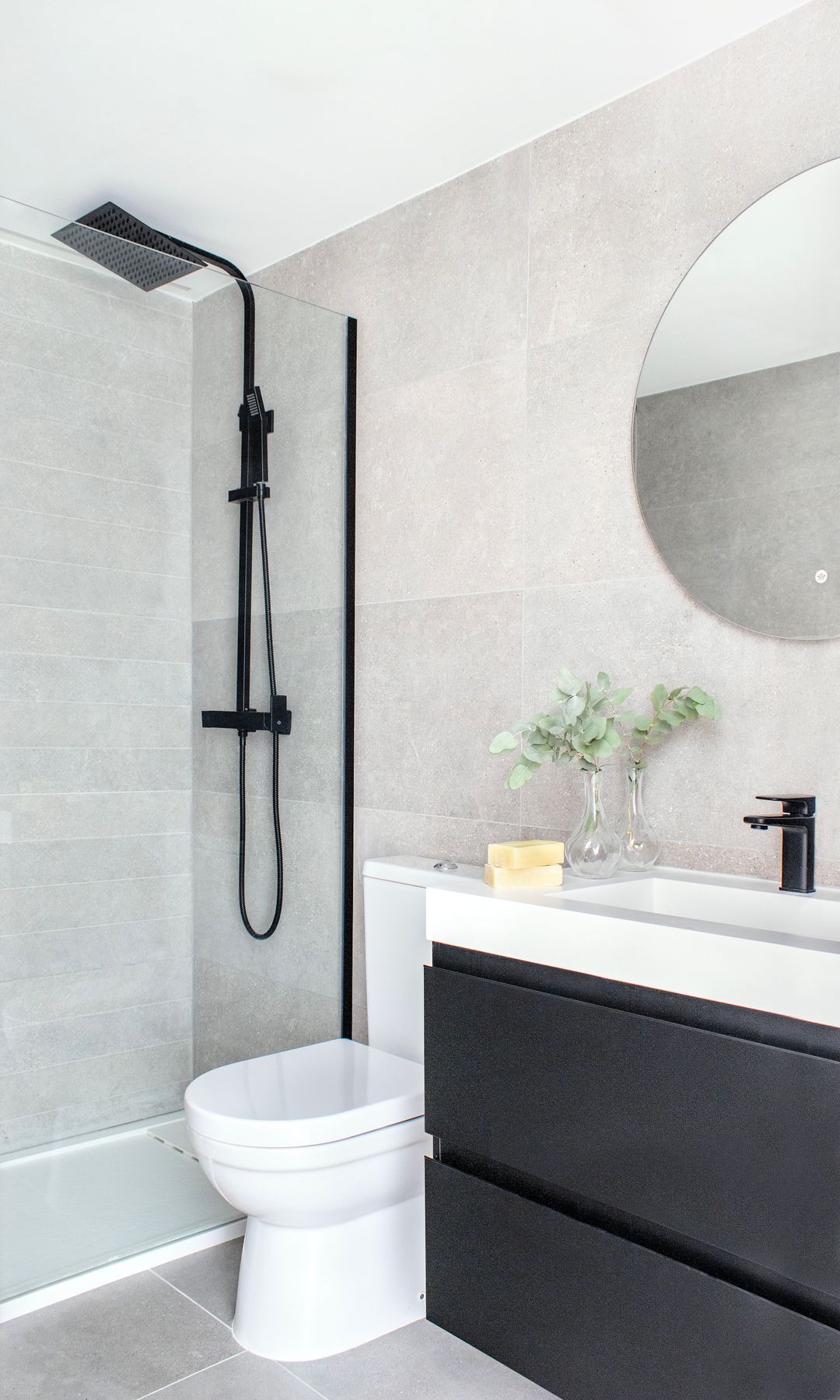 Baño con ducha, grifería negra, mampara con perfiles negros, espejo redondo, mueble bajolababo negro