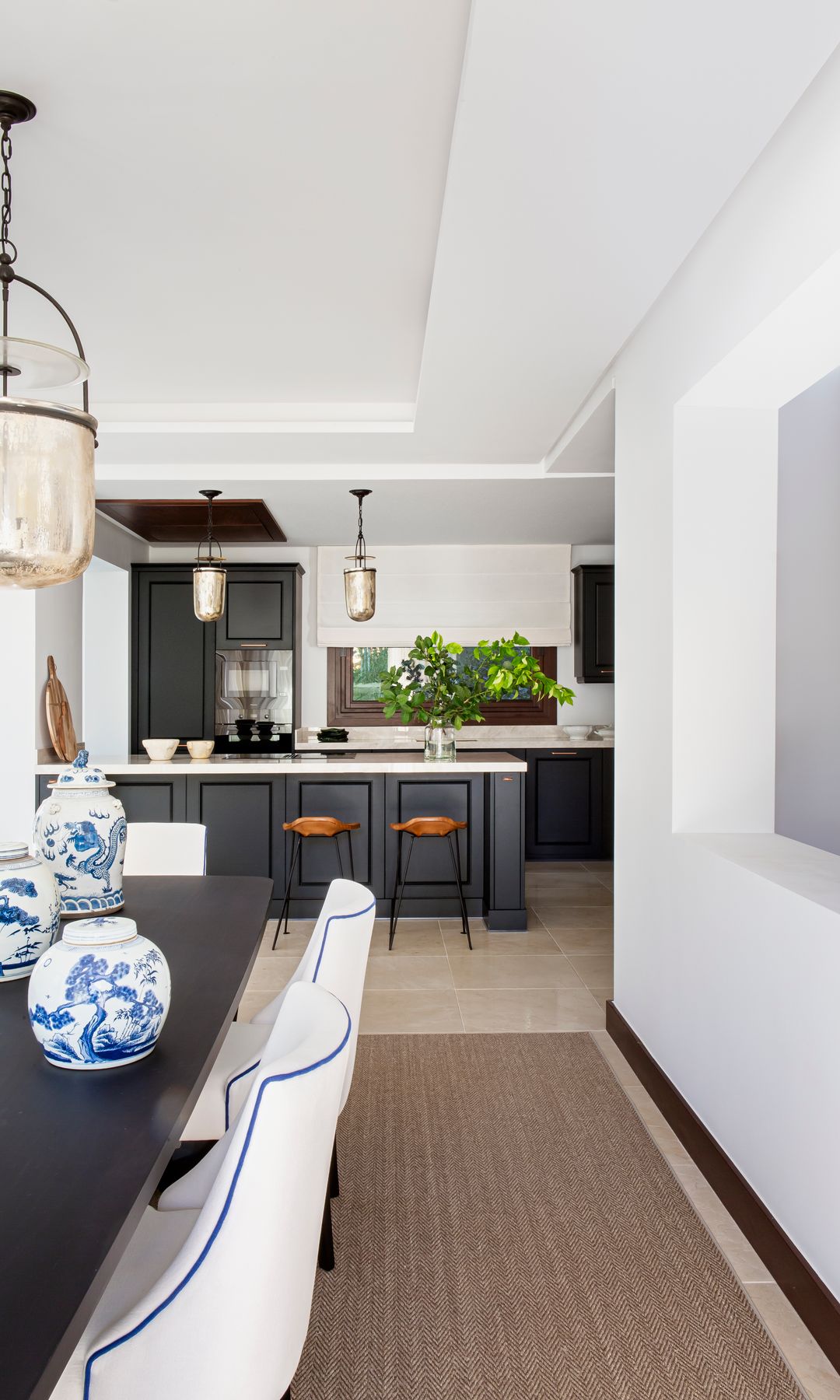 Cocina negra con comedor, con mesa oscura, jarrones de porcelana azules y blancos, alfombra y lámpara de techo