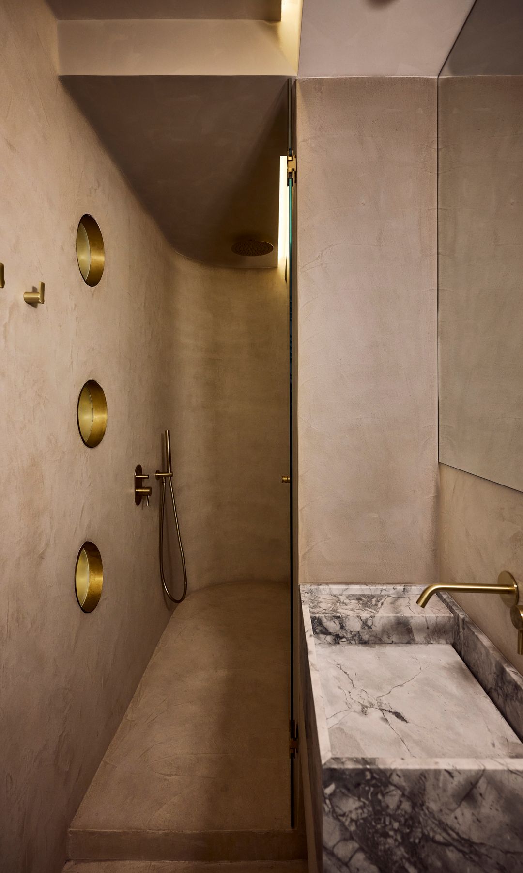 Baño con paredes con textura con acabado a la cal, lavabo de piedra y grifería dorada 
