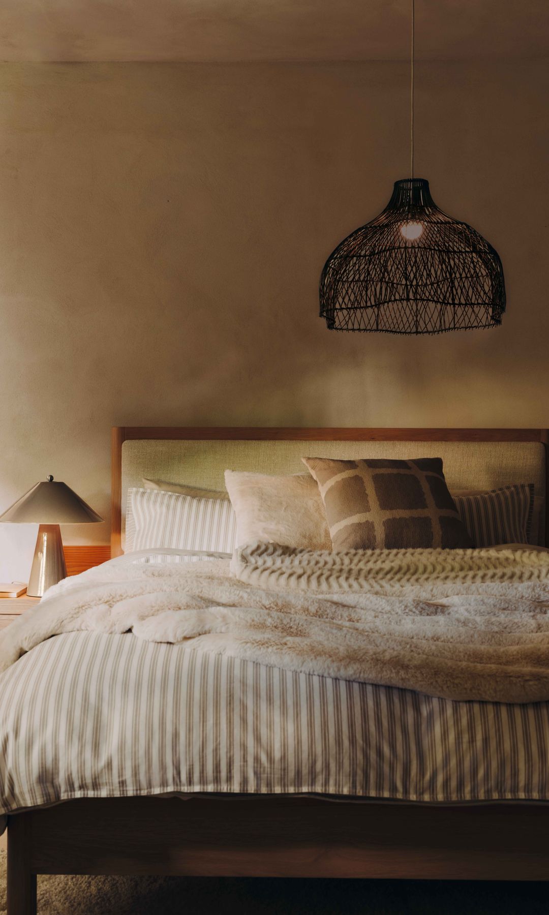 Dormitorio con cabecero de madera tapizado, lámpara de techo, funda de rayas beige