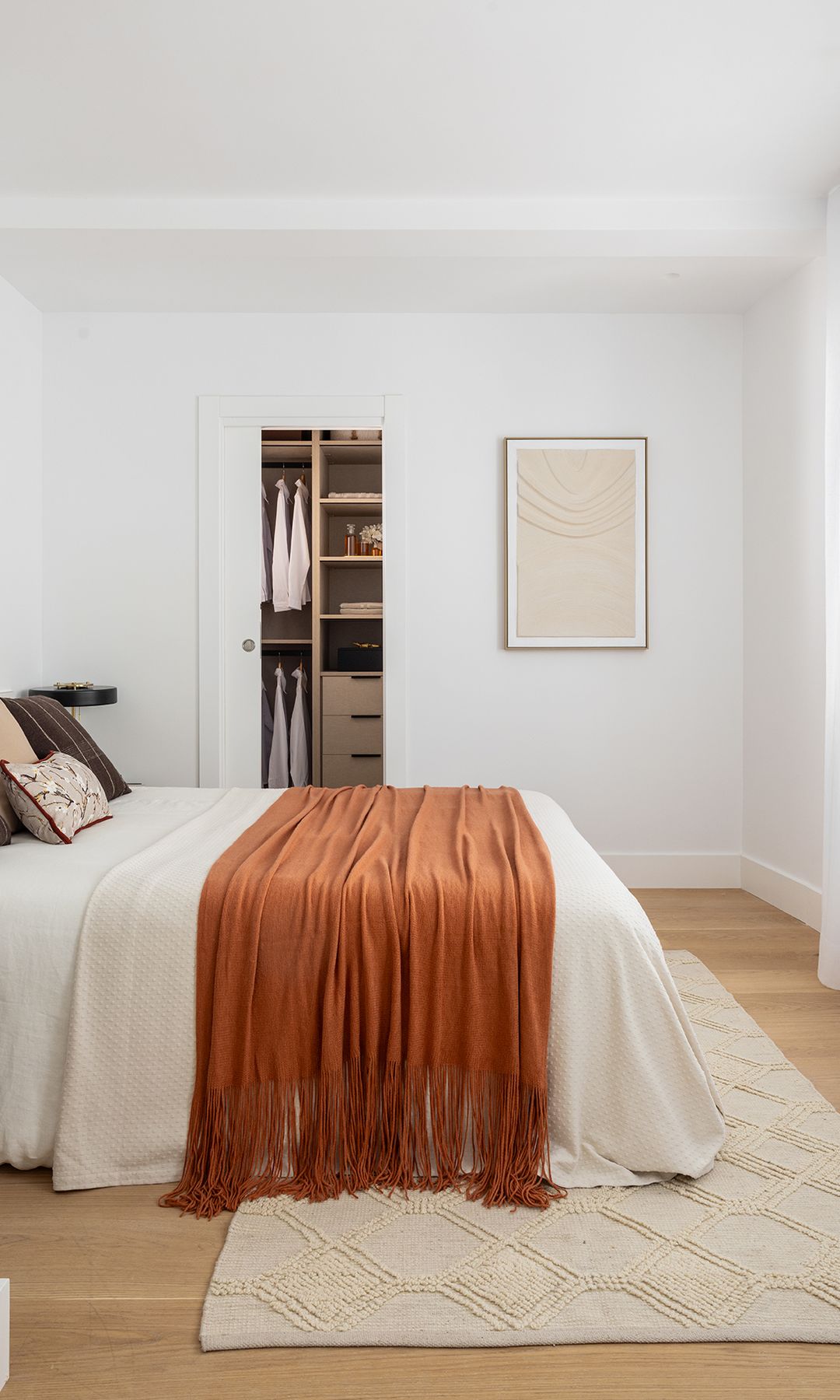 Dormitorio con vestidor y cortinas blancas ligeras, ropa de cama en tonos tierra y alfombra 