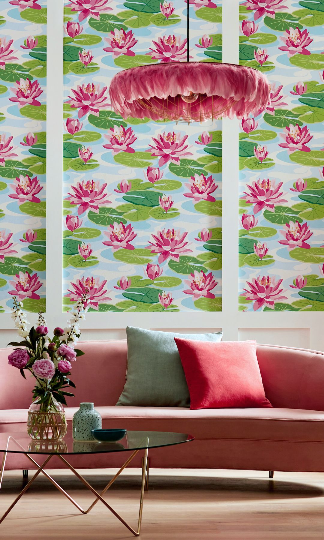 Salón con sofá rosa, papel pintado verde y rosa, mesa de centro de cristal, lámpara de plumas rosa