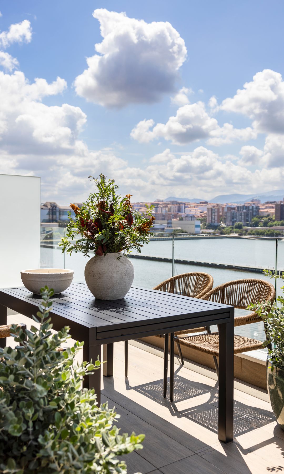 Terraza con comedor con mesa de madera, sillas de fibras vegetales y macetas con plantas