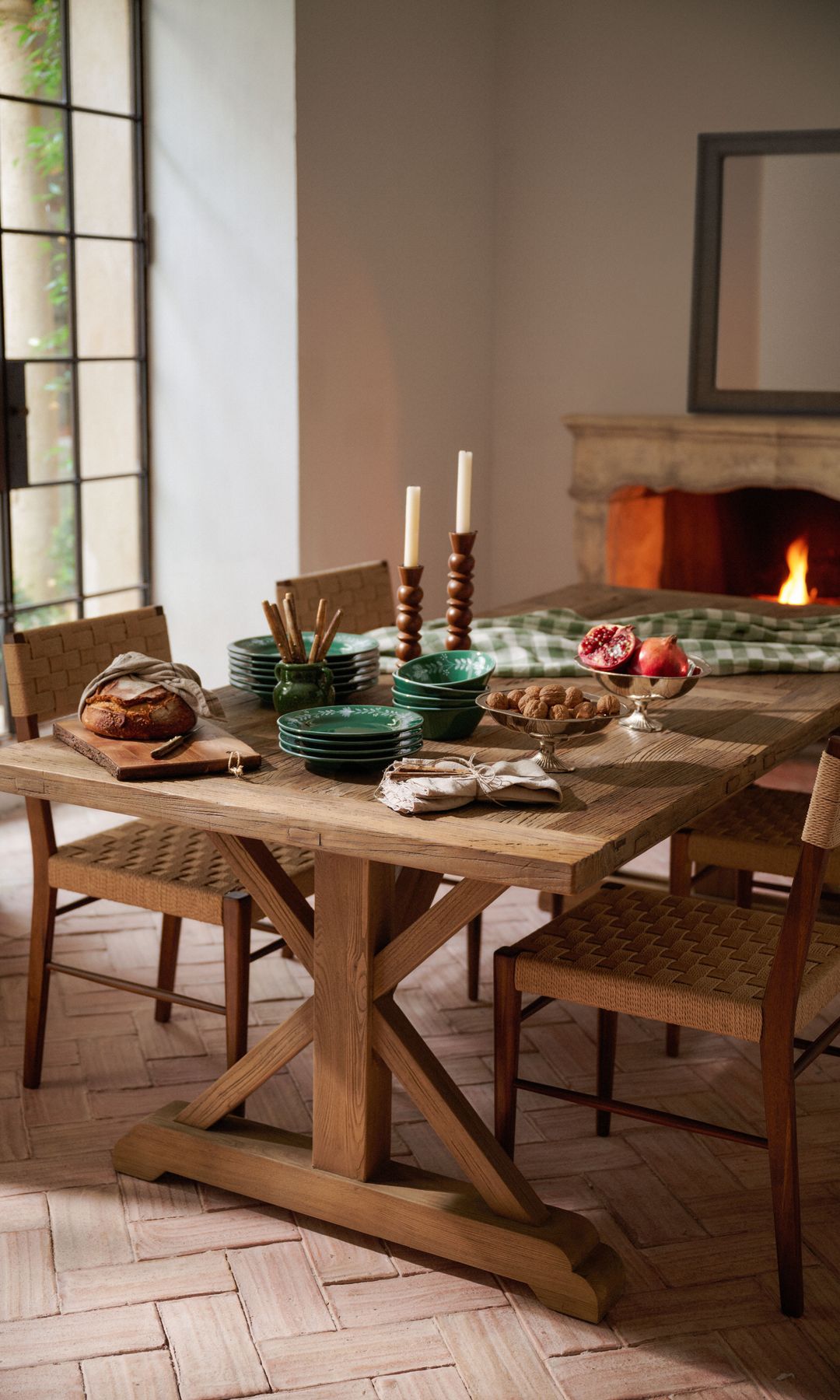 Comedor con chimenea, mesa de madera, cuadro sobre la chimenea, suelo de barro, vajilla porcelana verde, candelabros, fruta