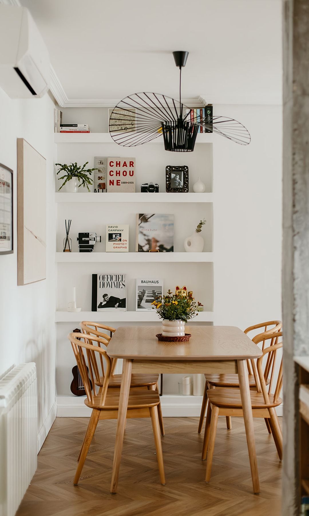Comedor con suelo de madera, mesa y sillas de madera, estantería de obra, cuadros y radiador