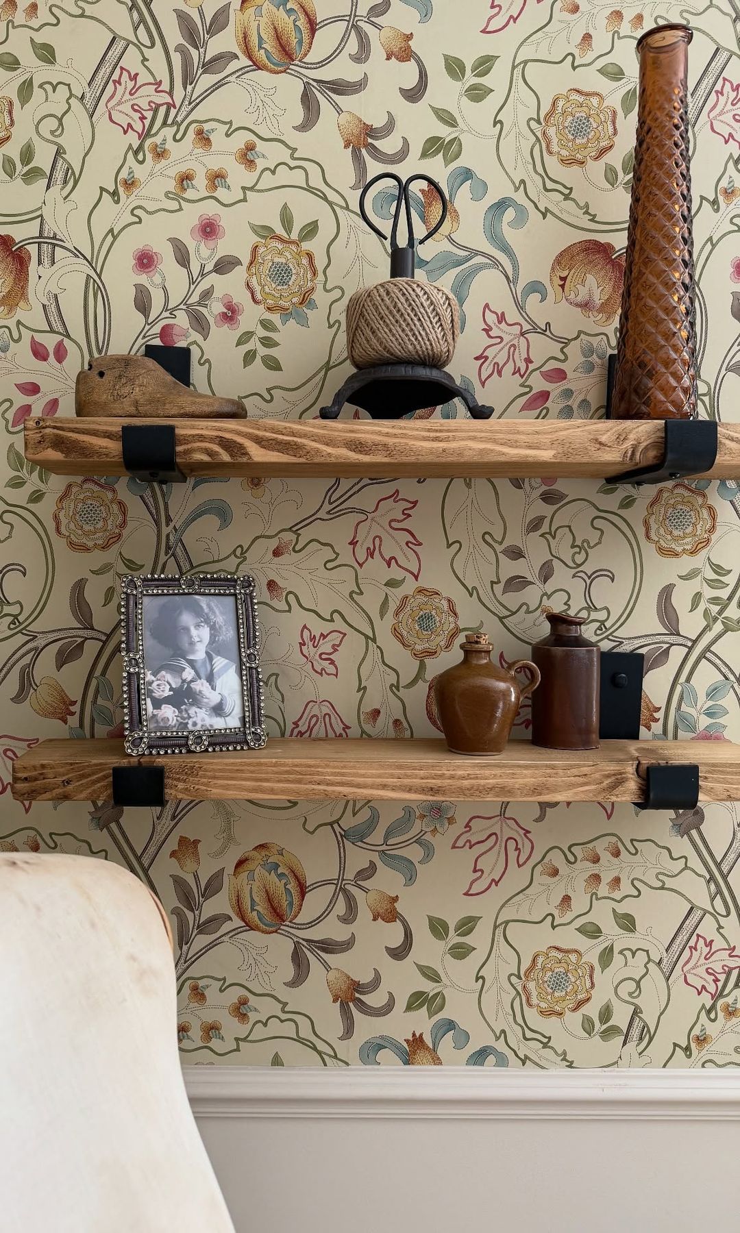 Pared con papel pintado de flores en tonos claros, baldas de madera, con adornos y una foto antigua