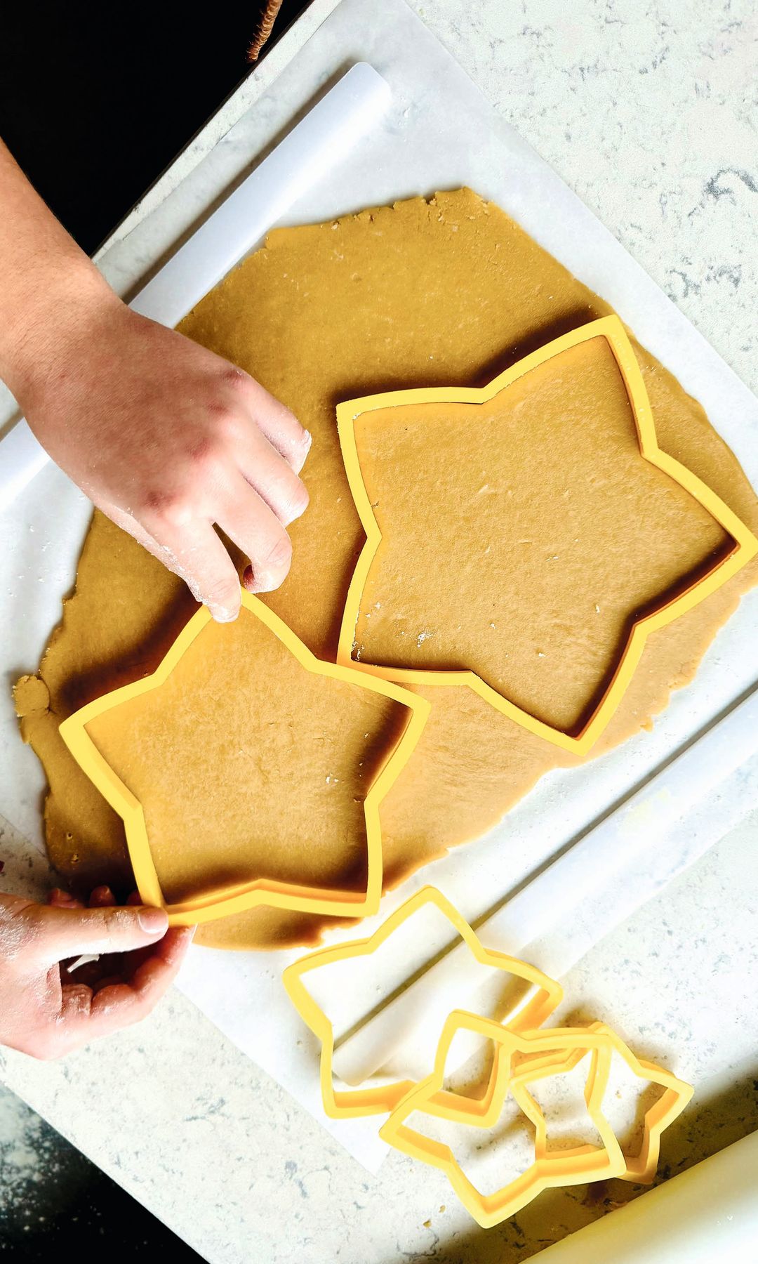 Manos cortando masa con cortadores de estrella. Tres cortadores a un lado.