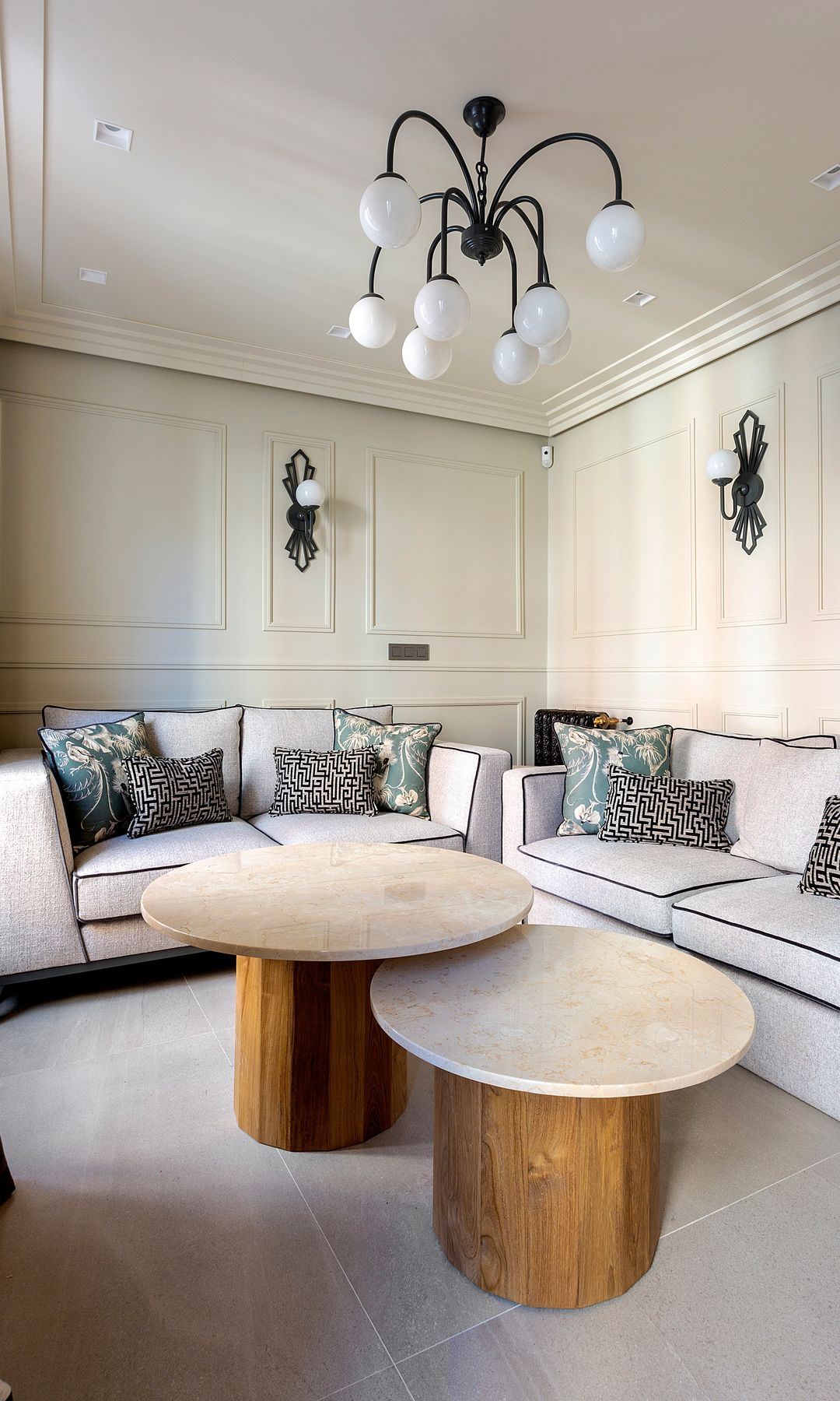 Salón con molduras en la pared, lámpara de techo, apliques de pared negros, sofás blancos con ribete negro, mesas de centro, cojines