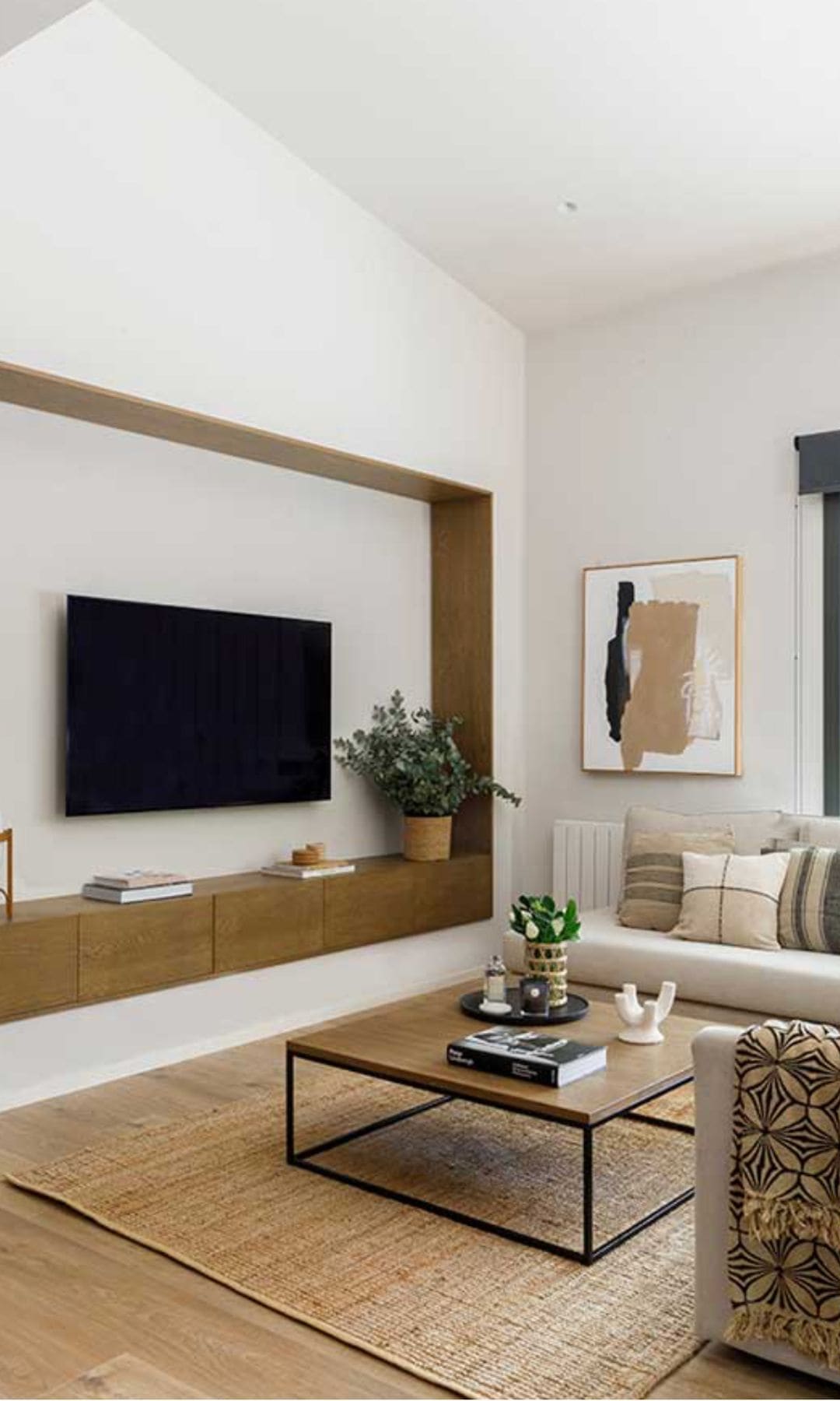 Salón con televisión colgada en la pared, mueble tipo hornacina en madera con cajones, mesa de centro, alfombra de fibras vegetales