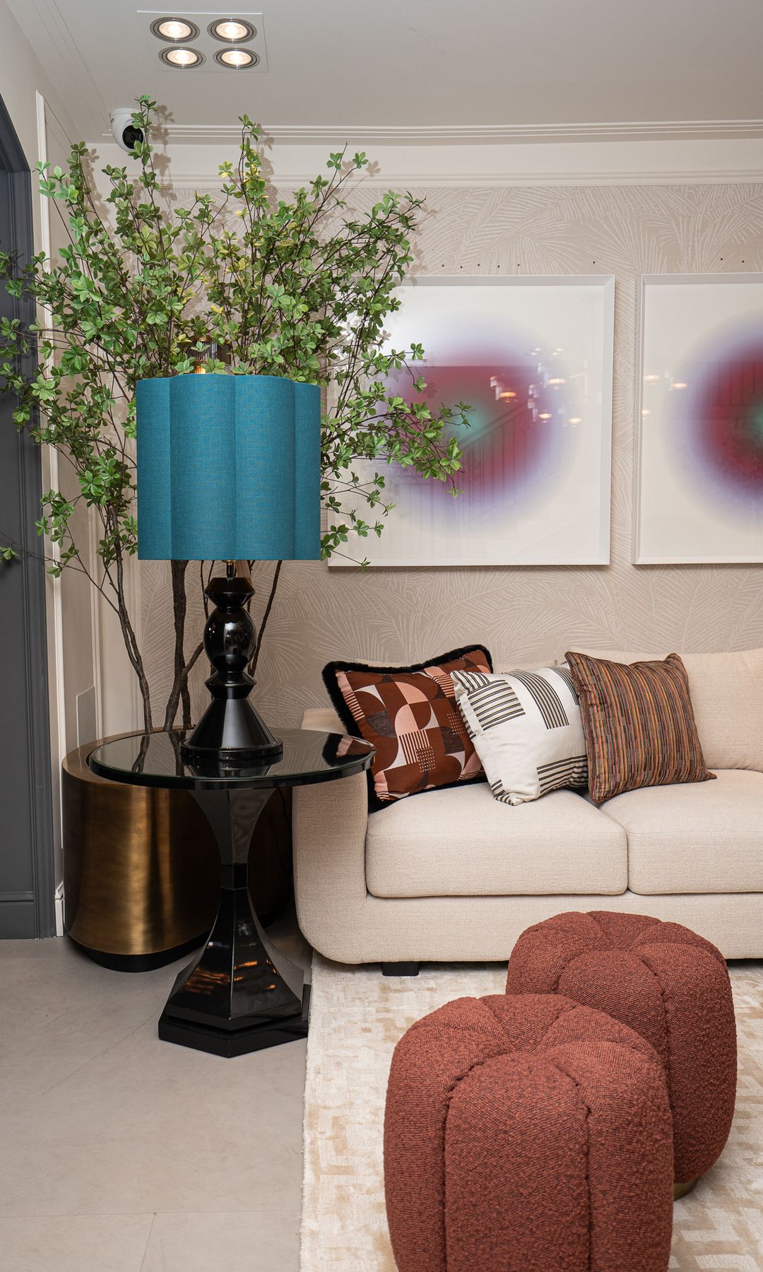 Salón con sofá blanco, cojines de colores y cuadros en la pared del sofá, mesa auxiliar negra, lámpara de sobremesa azul, árbol en maceta