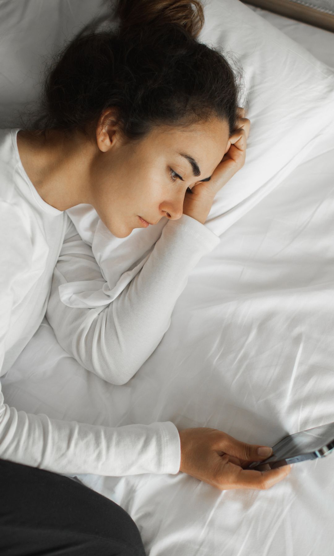 mujer en la cama, despierta mirando el móvil, sin poder dormir