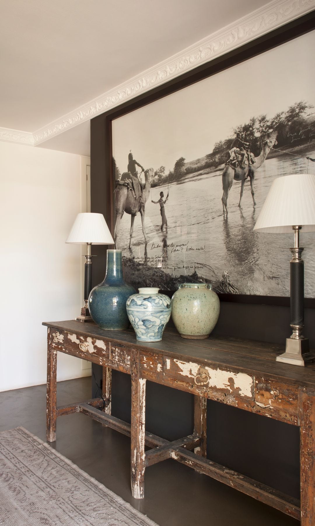 Recibidor con consola antigua, foto en blanco y negro XL colgada en la pared, lámparas de sobremesa, vasijas, alfombra