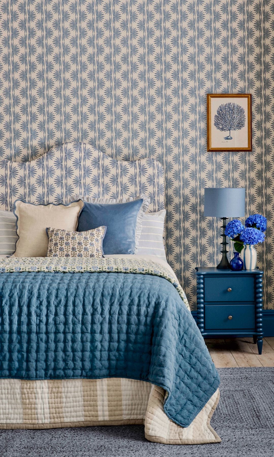 Dormitorio con papel pintado azul, cabecero tapizado a juego, mesita e noche azul, jarrón con hortensias azules, lámpara de sobremesa azul, cojines y funda nórdica azul