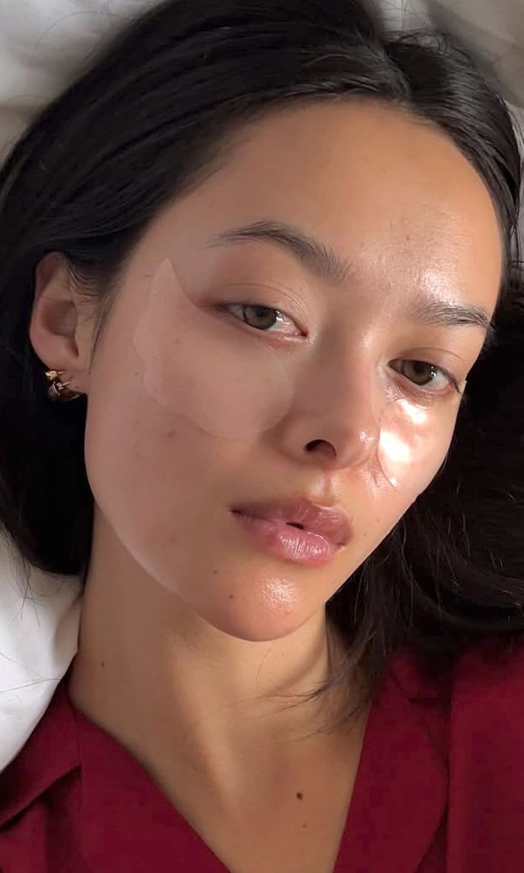 Mujer con parches transparentes para ojos y rostro hidratado, tumbada sobre almohada blanca