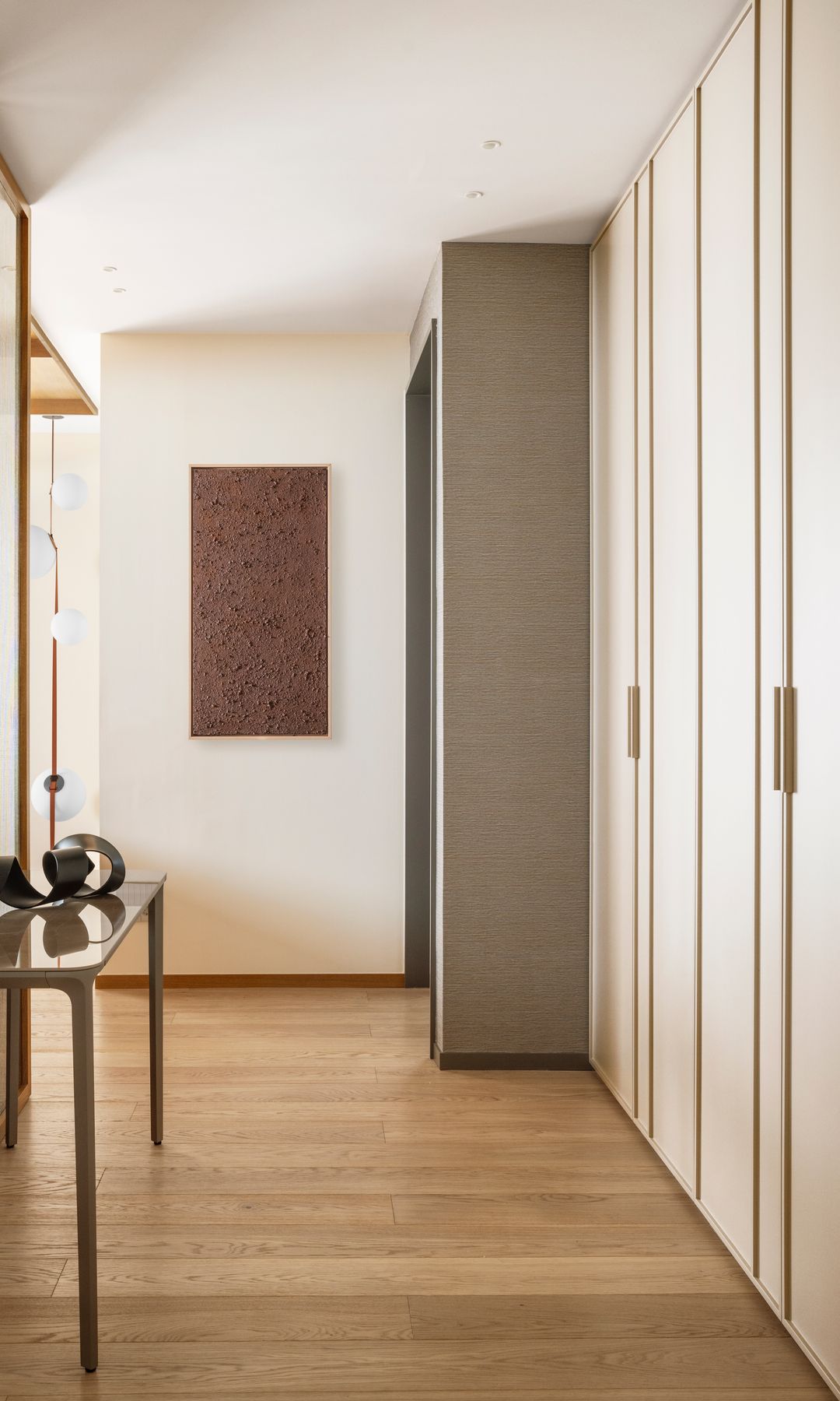 Pasillo con una pared de armarios, consola con lámpara de sobremesa, cuadro en la pared, suelo de madera