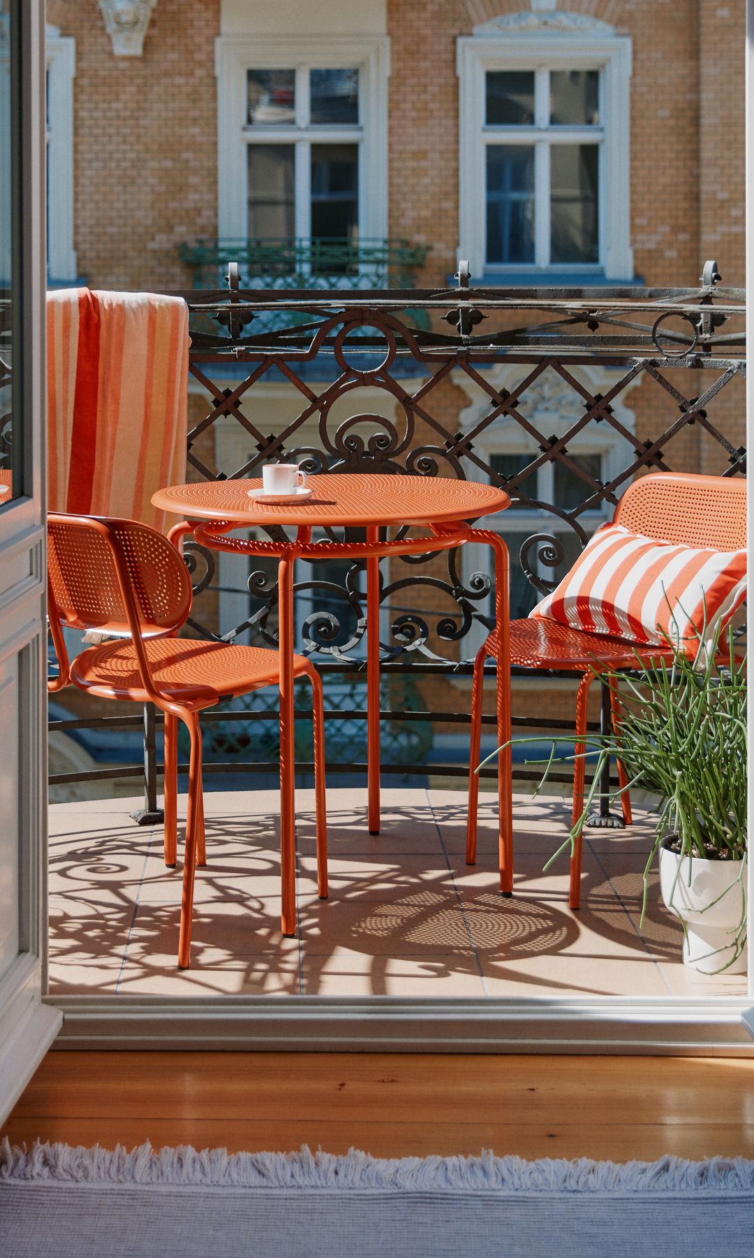 Balcón urbano con mesa y sillas de hierro en color naranja, maceta blanca en el suelo