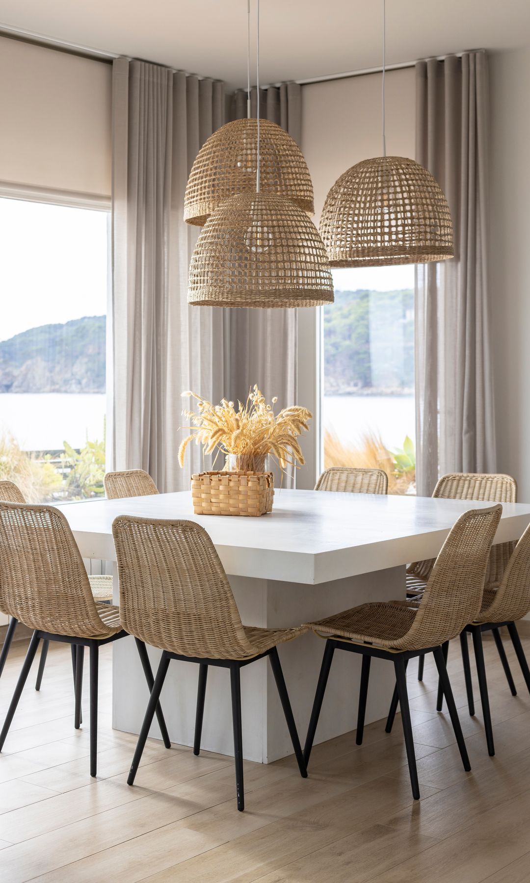Comedor con suelo porcelánico efecto madera, mesa blanca cuadrada, sillas de fibras vegetales, lámparas de techo de fibras vegetales