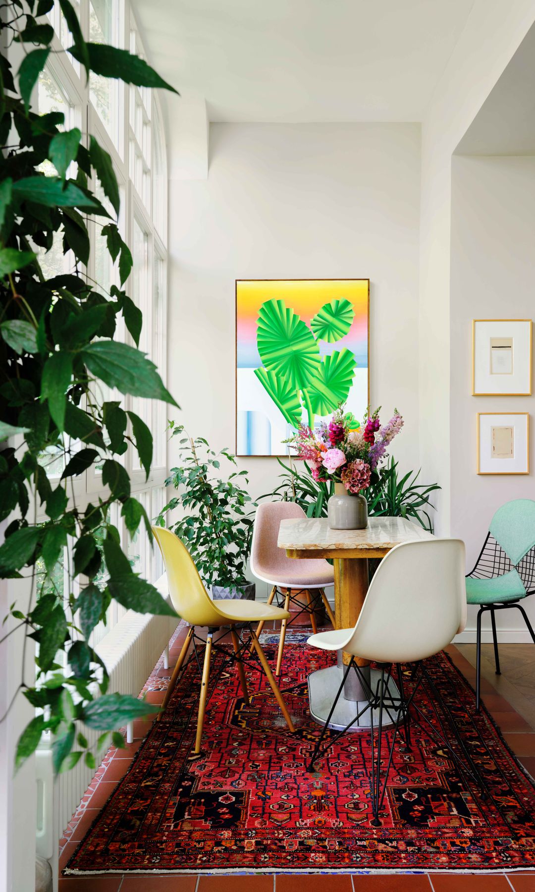 Comedor en una galería con mesa con el sobre de mármol, alfombra roja y plantas y flores 