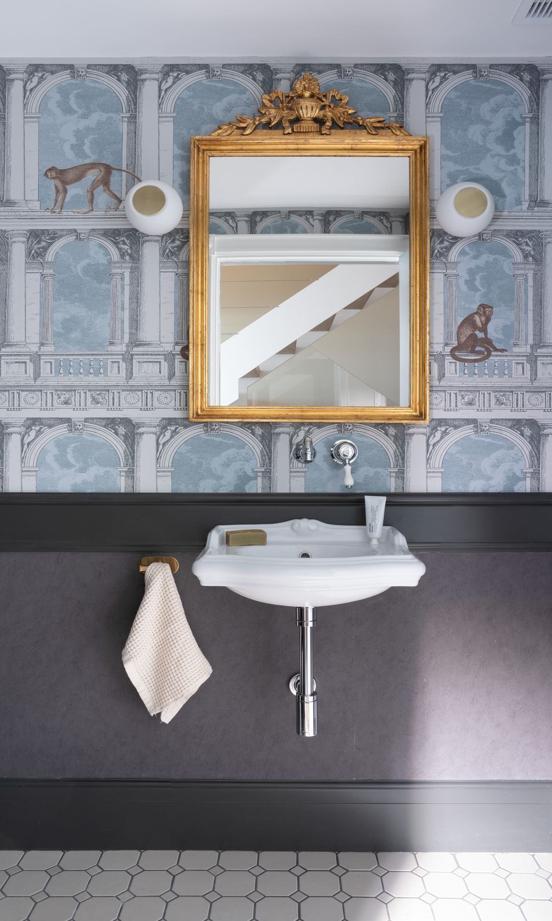 Baño con papel pintado, zócalo alto en negro, espejo dorado, lavabo empotrado, suelo porcelánico 