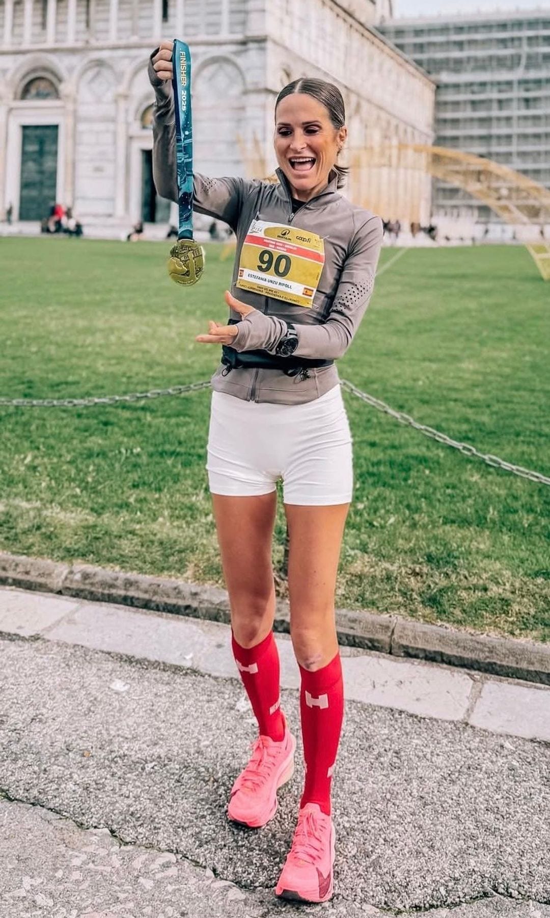Verdeliss con camiseta gris, shorts blancos y calcetines rojos, sosteniendo una medalla.