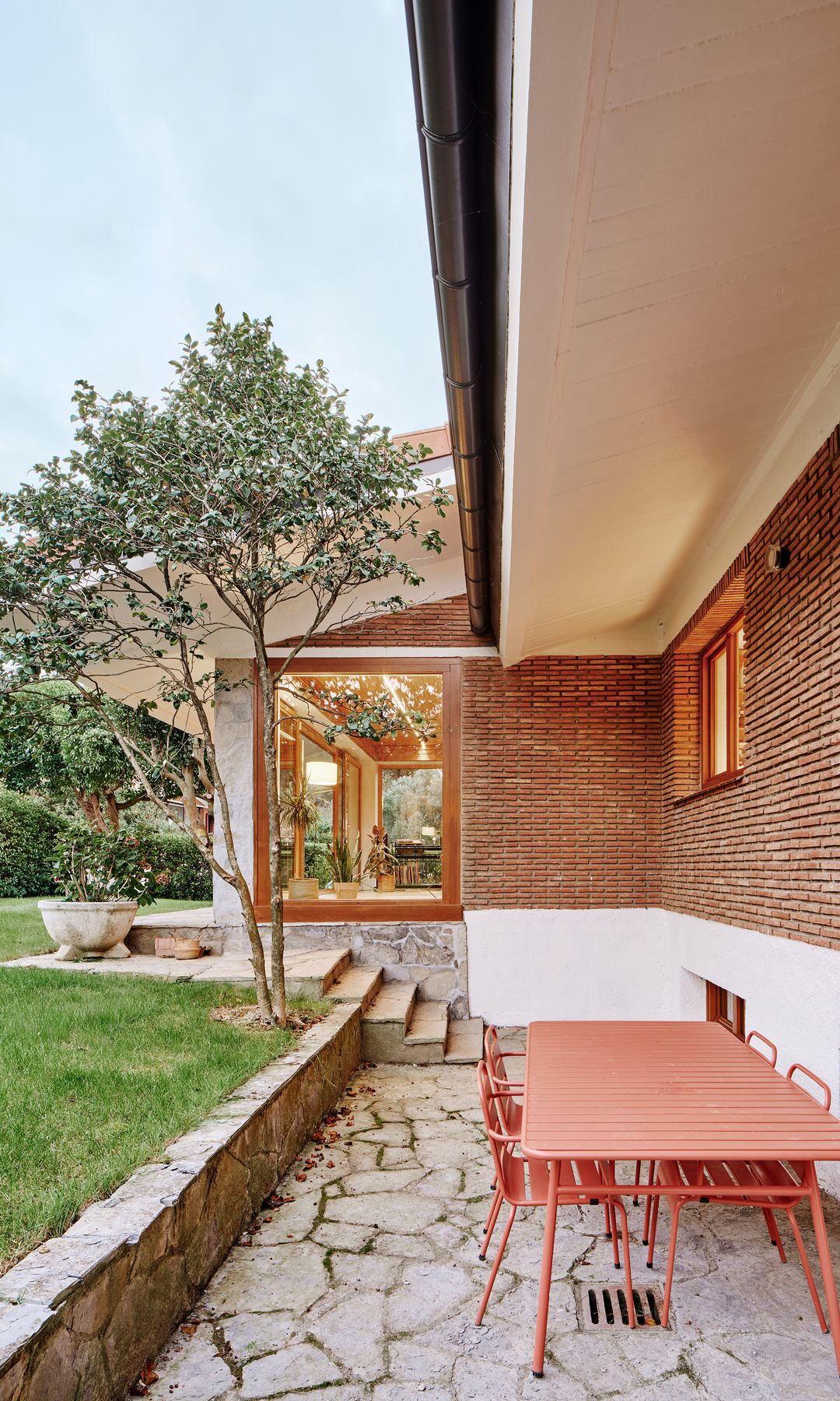 Exterior casa de ladrillo con jardín con césped, mesa naranja y sillas 