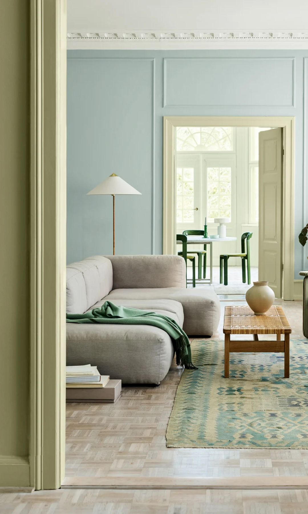 Salón comunicado con el comedor con paredes verdes en el recibidor y azul claro en el salón, techo blanco, alfombra en tonos verdes y azules, sofá gris, mesa de centro de madera