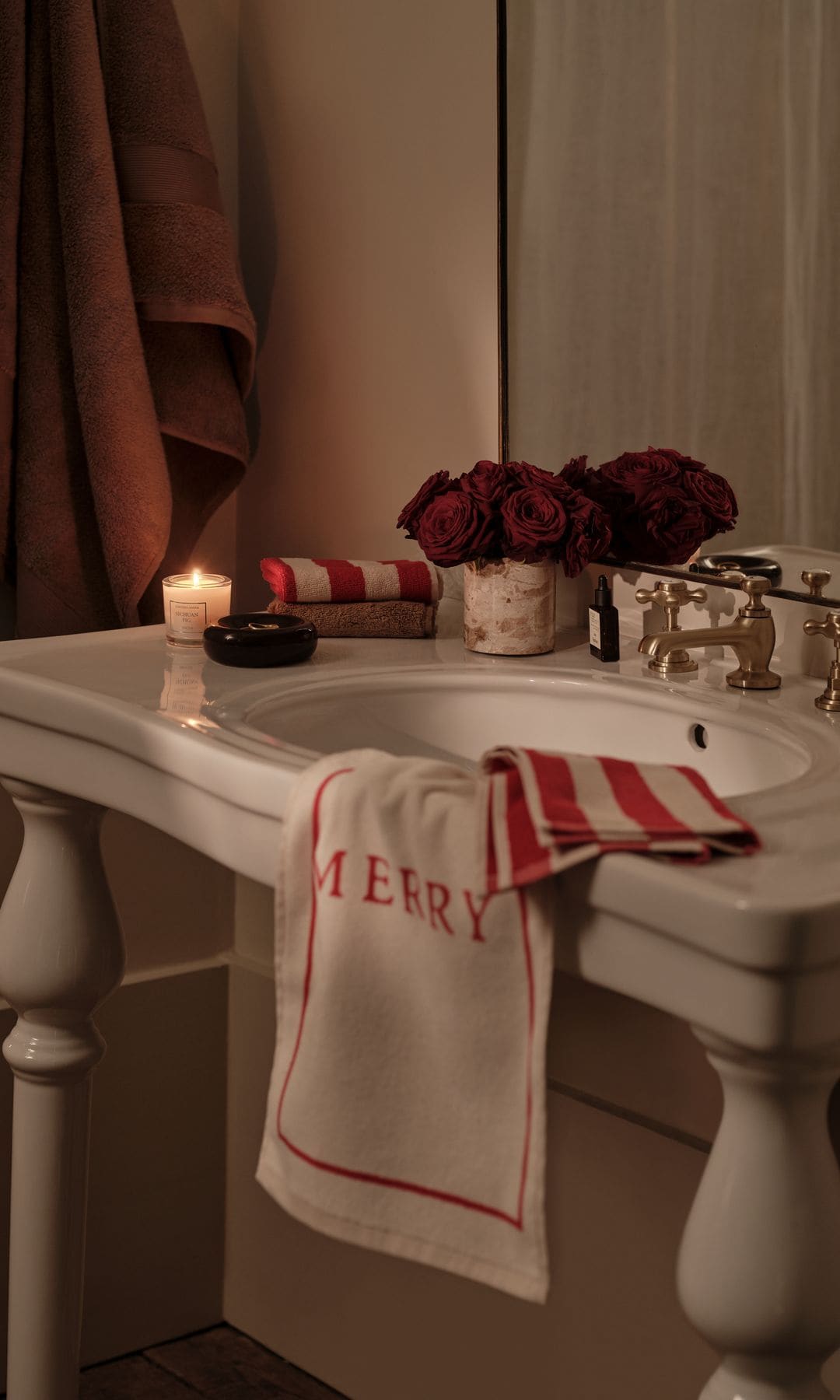 Baño decorado de Navidad, con lavabo de pie de color blanco antiguo, toallas con mensajes navideños, velas, arreglo floral rojo