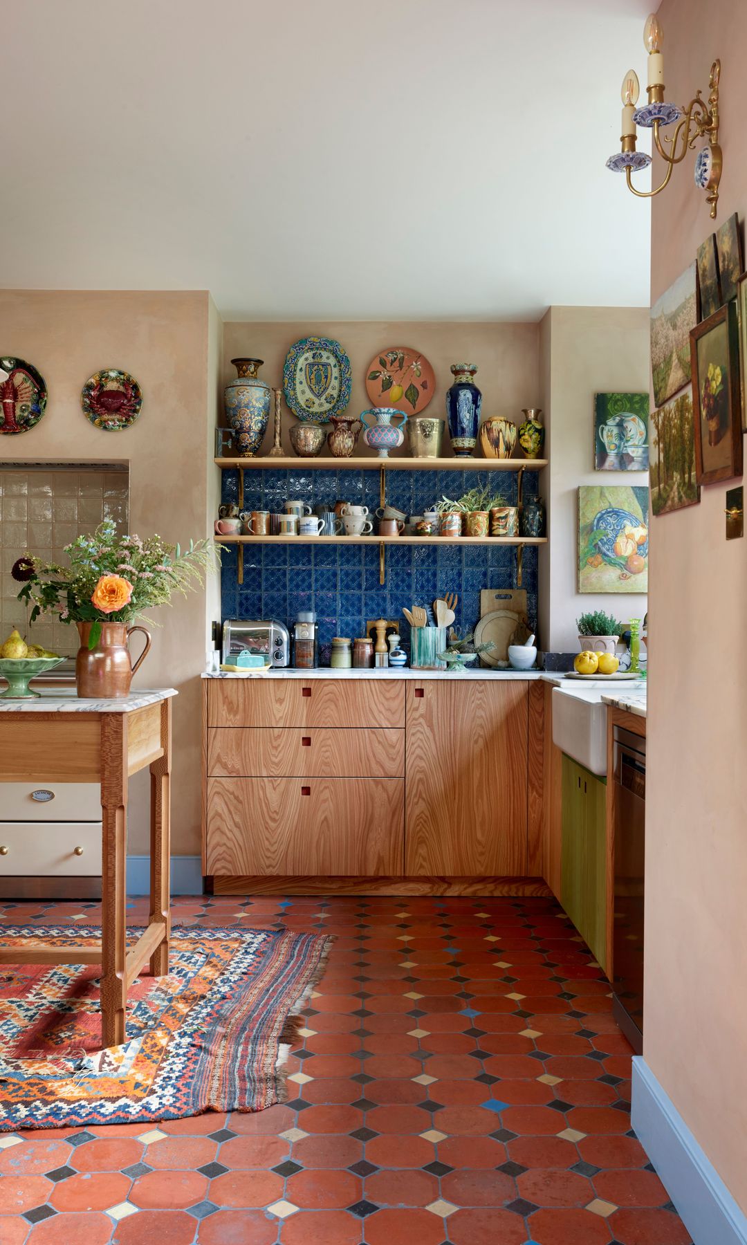 Cocina vintage con suelo de barro, pared de azulejos azules baldas con jarrones, cuadros y piezas de cerámica, mesa de cocina, alfombra