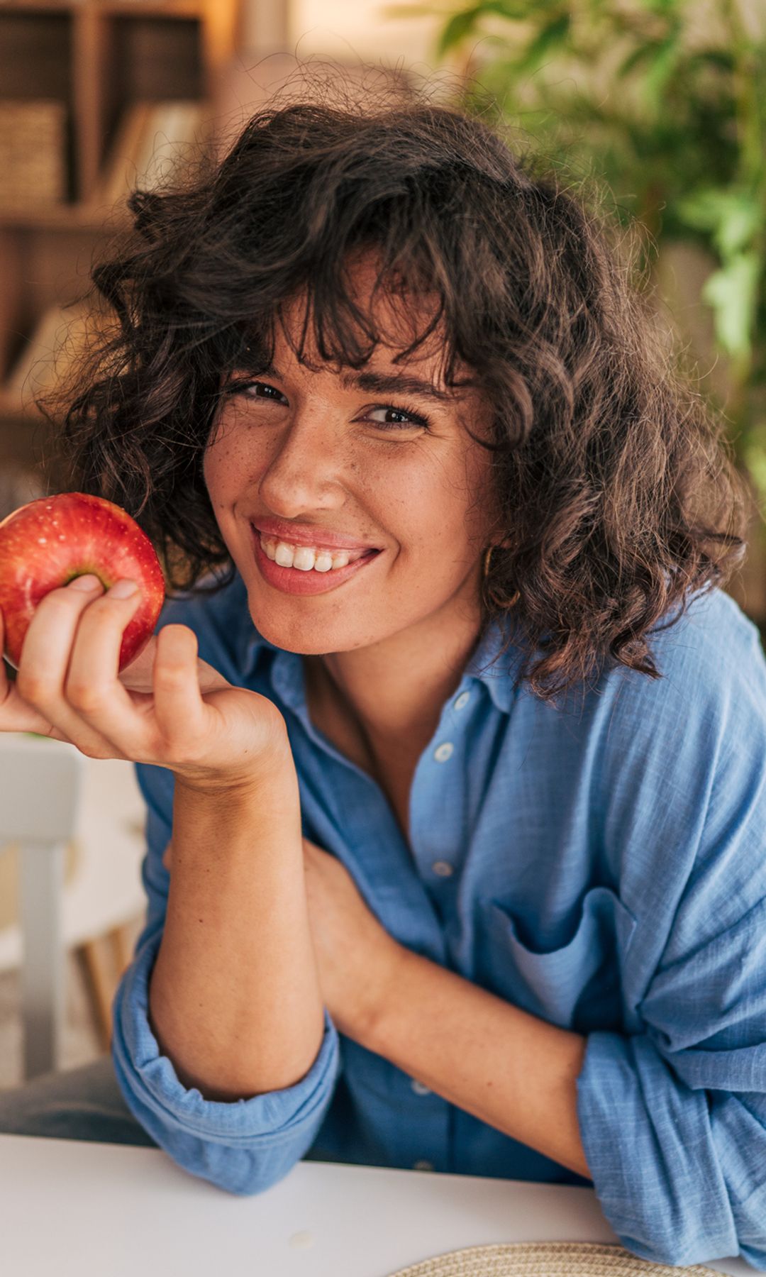 Mujer sonriente comiendo una manzana en el salón de su casa 