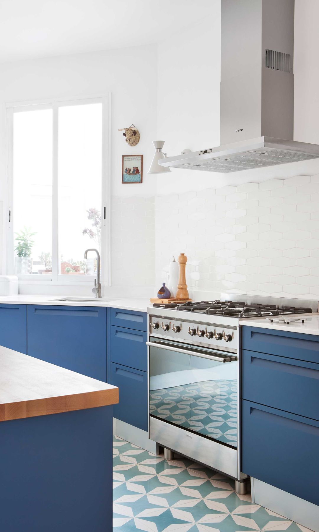 Cocina con muebles azules, paredes blancas, suelo damero en blanco y azul, campana de acero 