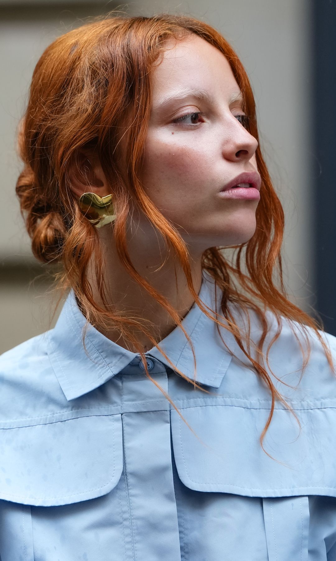 PARIS, FRANCE - JUNE 06: A guest wears a full Patou outfit with a light blue button-up shirt with a structured collar and oversized chest pockets. Hair is styled in loose waves, and earrings are visible, outside Patou,  on June 06, 2025 in Paris, France 