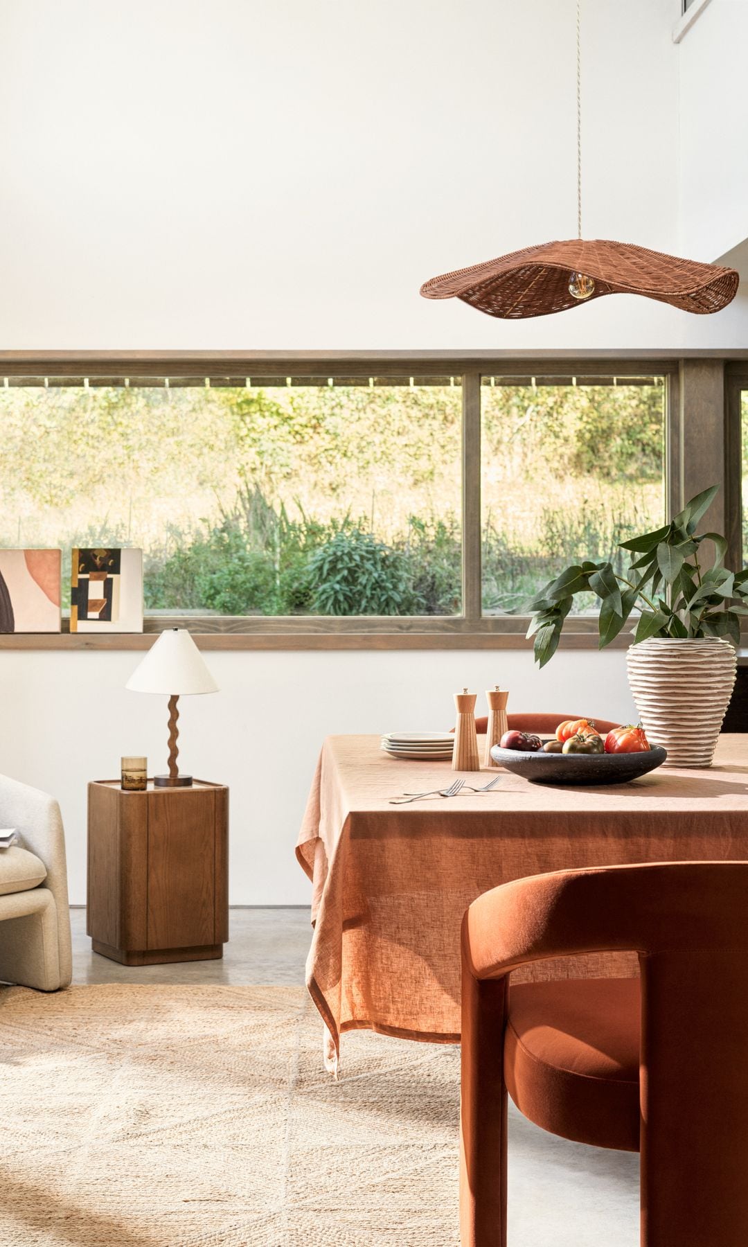 Salón comedor con lámpara de techo de fibras vegetales, mesa con mantel y jarrón, rincón junto a la ventana con butaca y mesa auxiliar con lámpara de sobremesa 