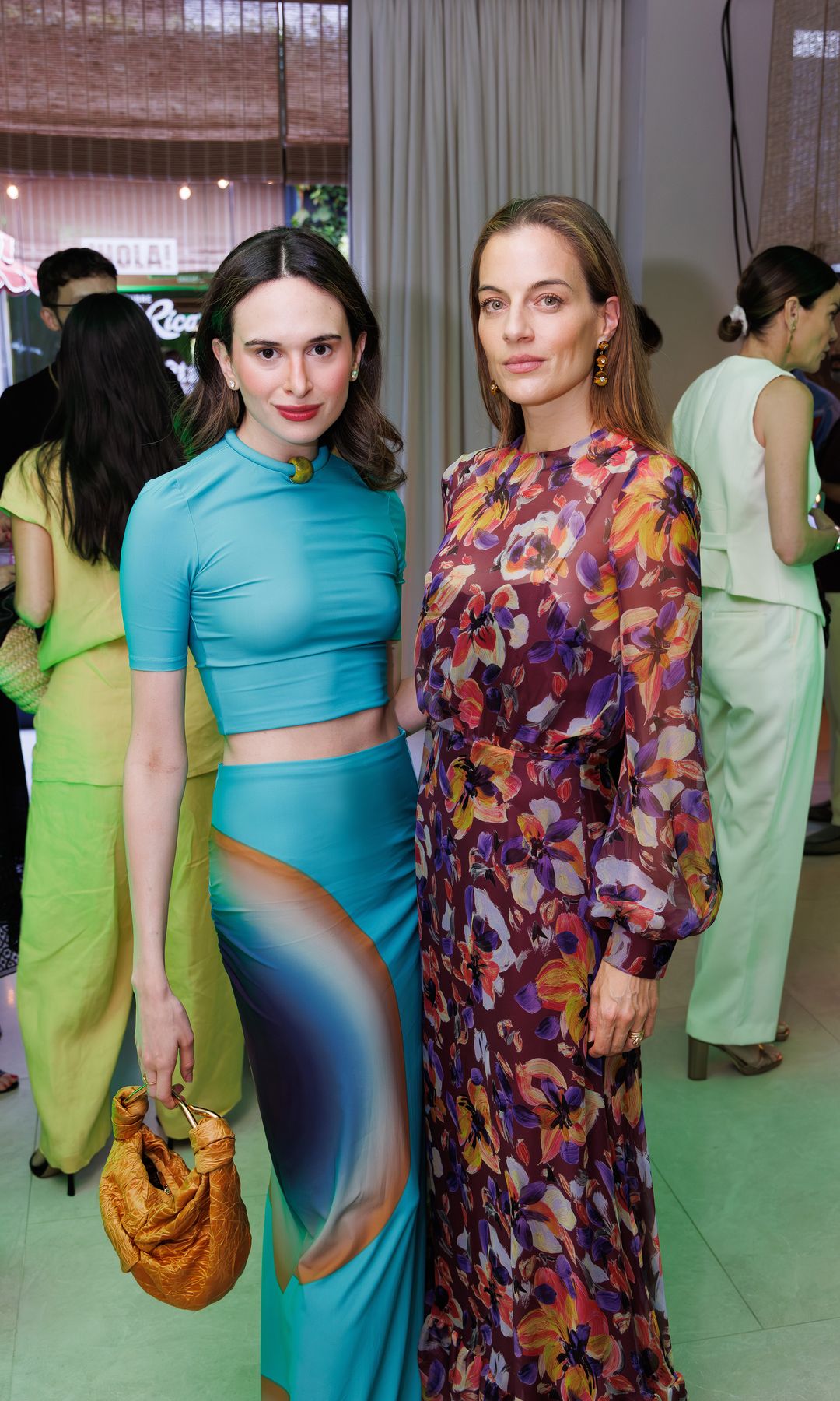 Dos mujeres en un evento, una en azul y otra en vestido floral, charlando.