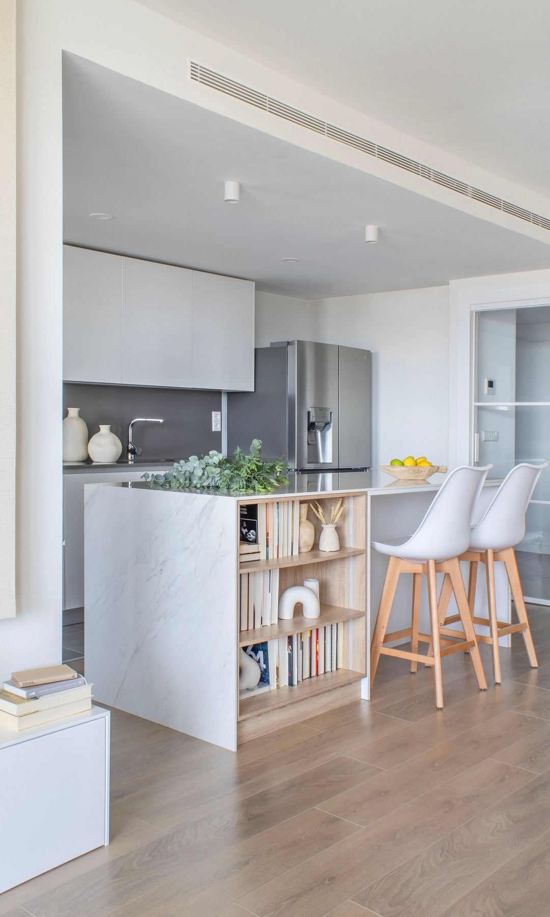 Cocina abierta con isla con zona abierta con estantería con libros, taburetes altos, electrodomésticos de acero