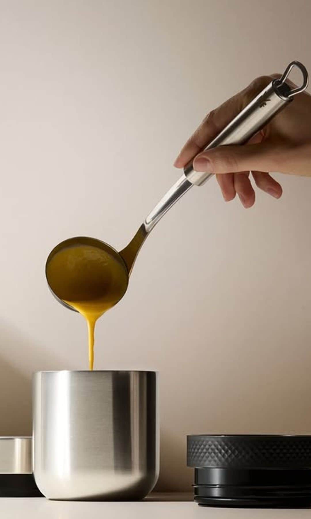 Mujer sirviendo una crema de calabaza con un cazo en un termo de acero inoxidable.