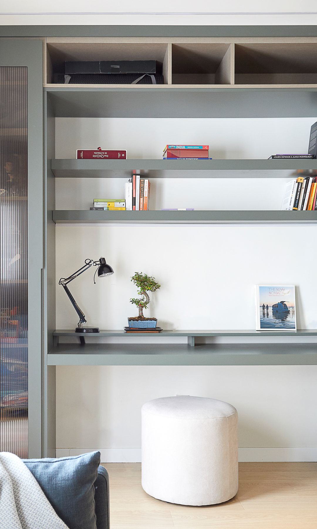 Rincón teletrabajo con escritorio gris, baldas grises, puff blanco, puerta de armario de cristal, flexo