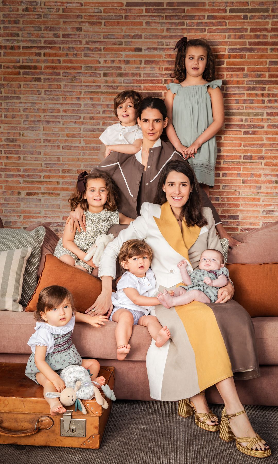 Las hermanas, con "looks" de su firma, con sus respectivos hijos, los cuatro de Inés y las dos niñas de Lucía: sentada sobre una maleta, la pequeña Lucía con "look" de Nícoli. En el sofá, Lucía madre abraza a Beltrán y a la pequeña Lola, ambos de Nícoli. Detrás, Inés rodeada por Casilda, con mono de flores de Coconut; Pelayo, con pantalón de Boboli y camisa de Nícoli, y, por último, Inés, con vestido de Nícoli y lazo en el pelo de Cóndor. Los peluches son de Pasito a Pasito