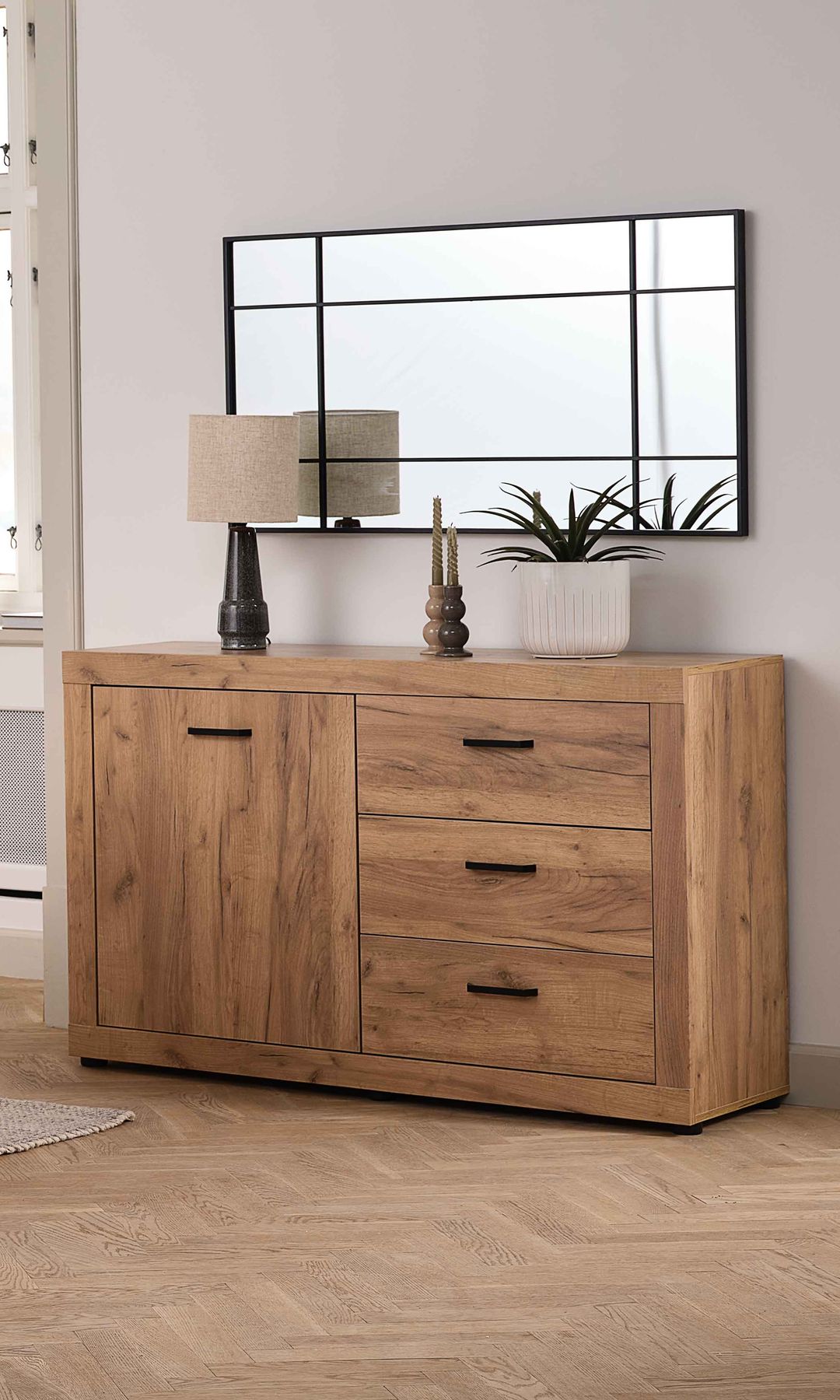 Comedor con aparador de madera, espejo rectangular con el marco negro, lámpara de sobremesa, maceta blanco con planta y vela