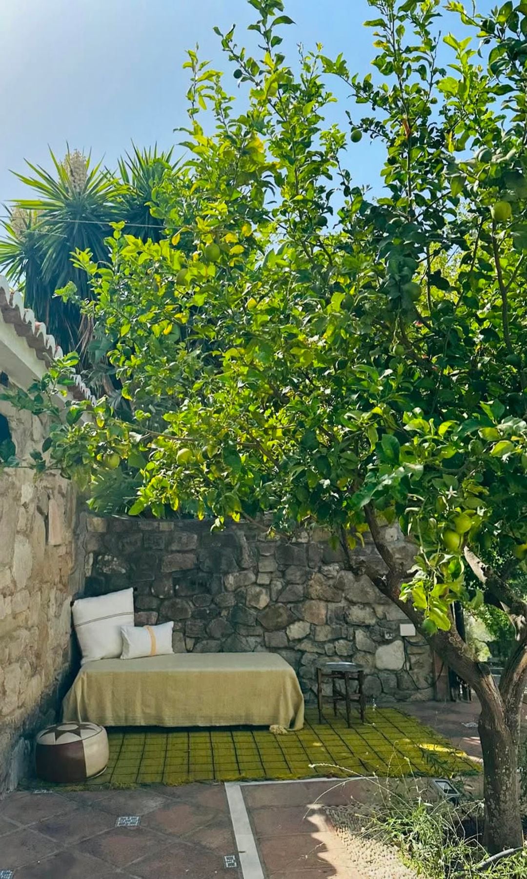 Casa de piedra con rincón del jardín con limonero, cama, alfombra y cojines