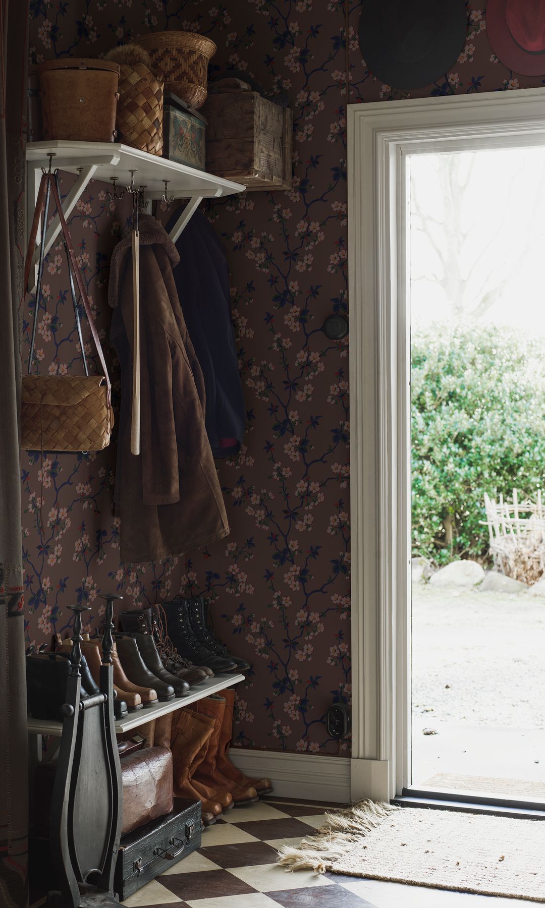 Recibidor de una casa de campo con suelo de damero en blanco y negro, papel pintado, banco, perchero de pared con balda superior de color blanco, paragüero