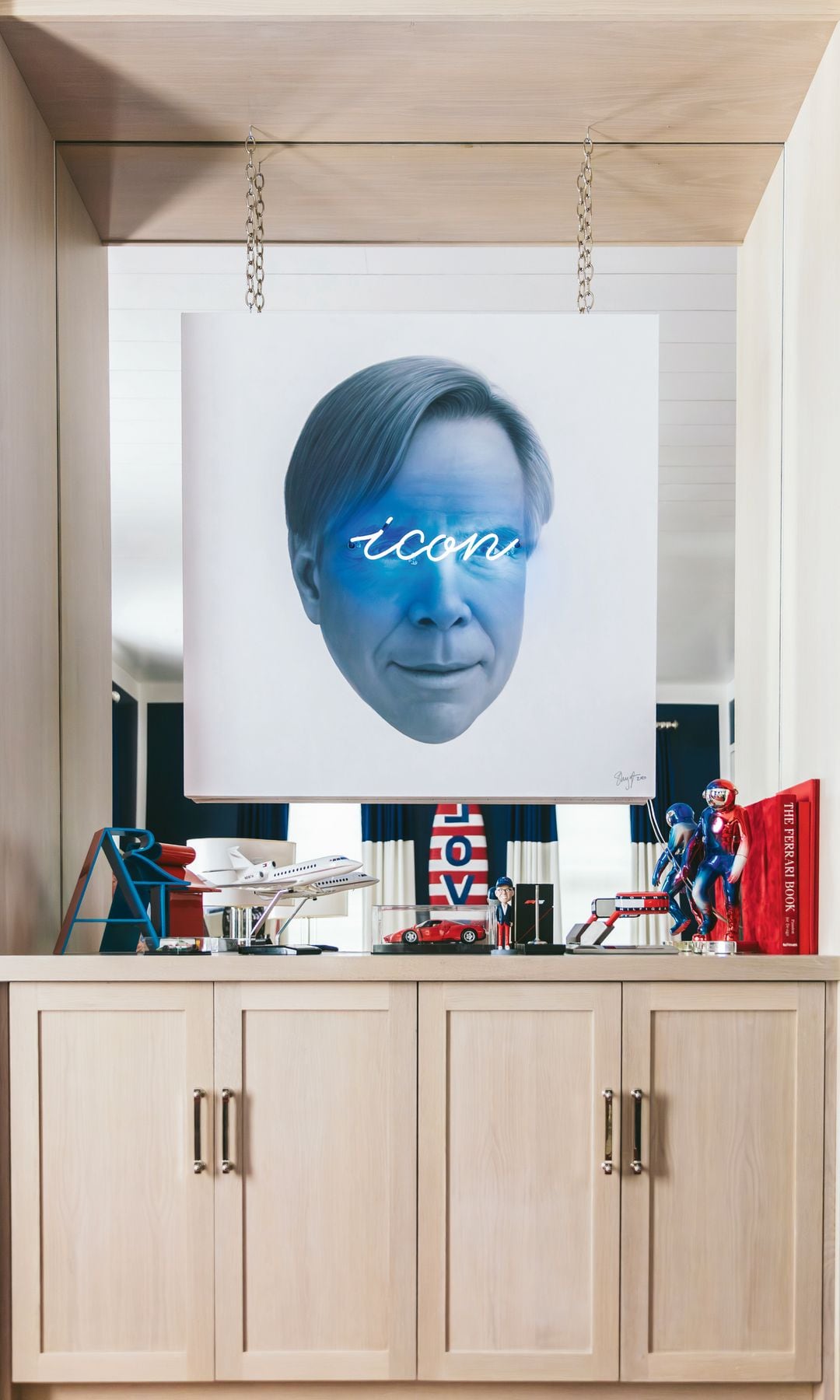 Imagen artística de videoinstalación de Shyglo con el retrato de Tommy Hilfiger colgada encima de un mueble de madera clara y diversos objetivos decorativos
