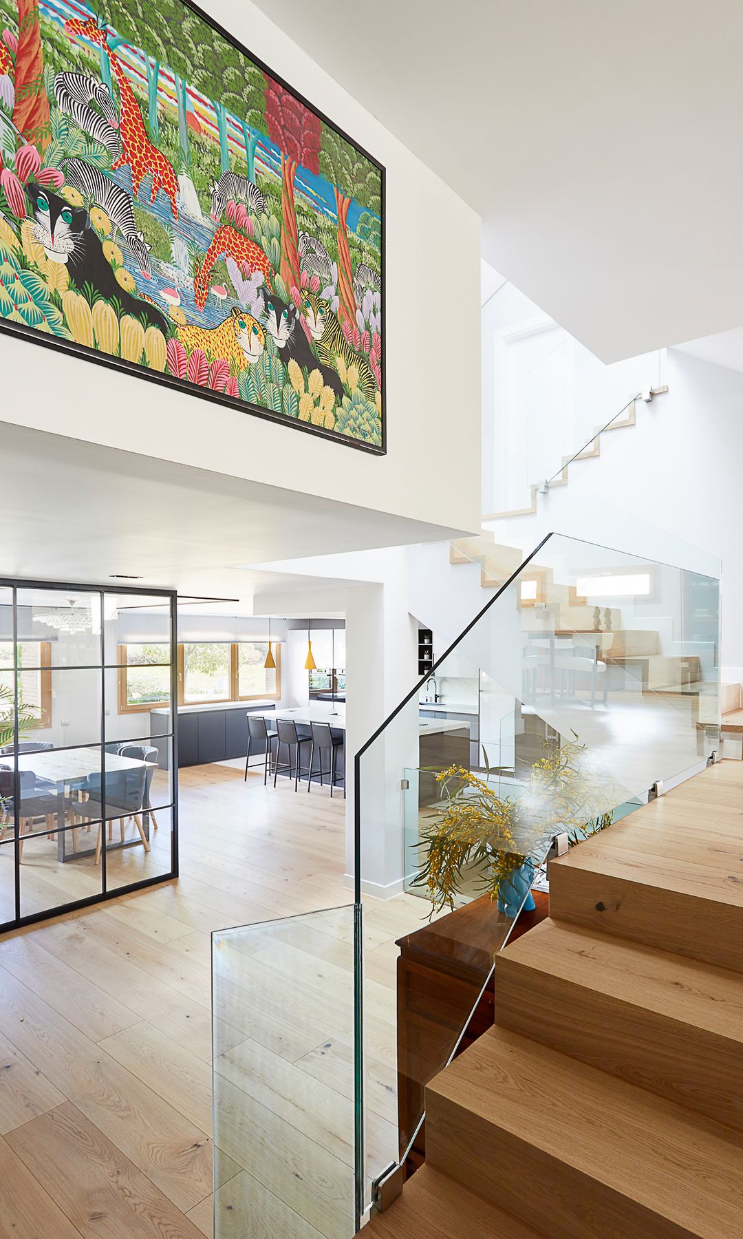 Escalera con barandilla de cristal abierta al salón comedor con tabique de cristal, gran cuadro en la pared