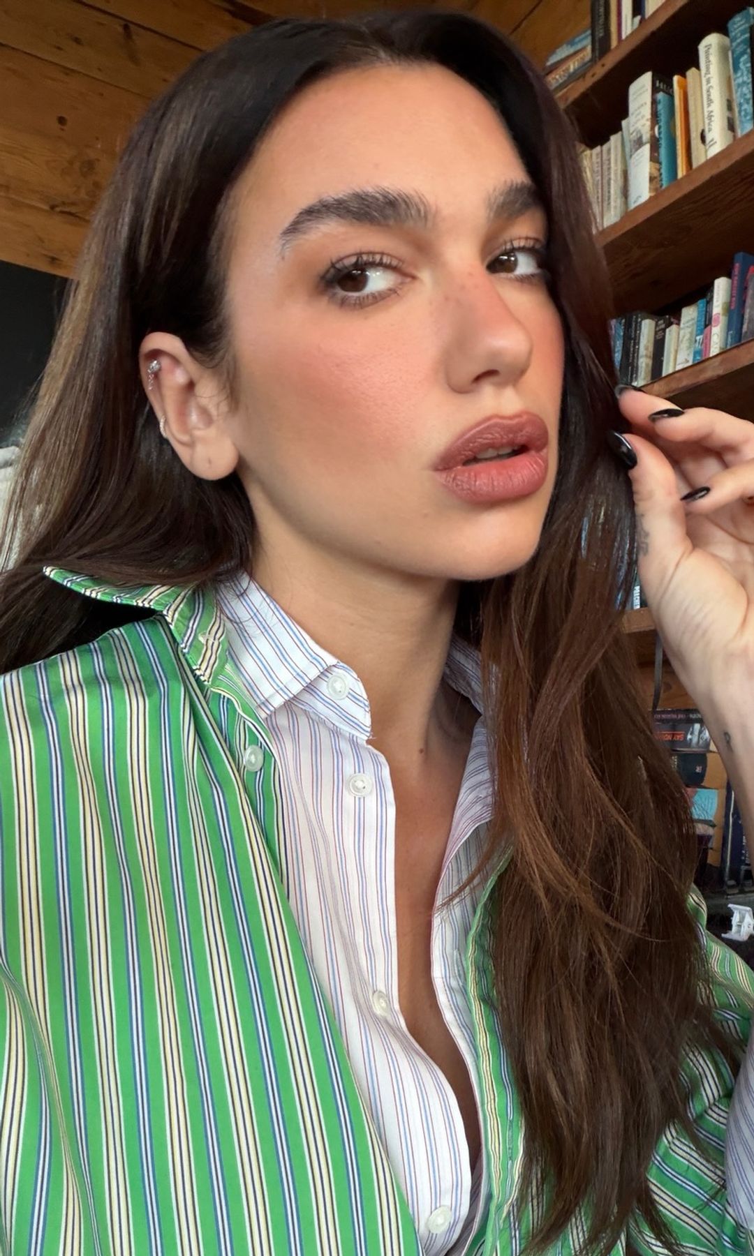 Dua Lipa con pelo suelto ondulado, labios maquillados y dos camisas superpuestas