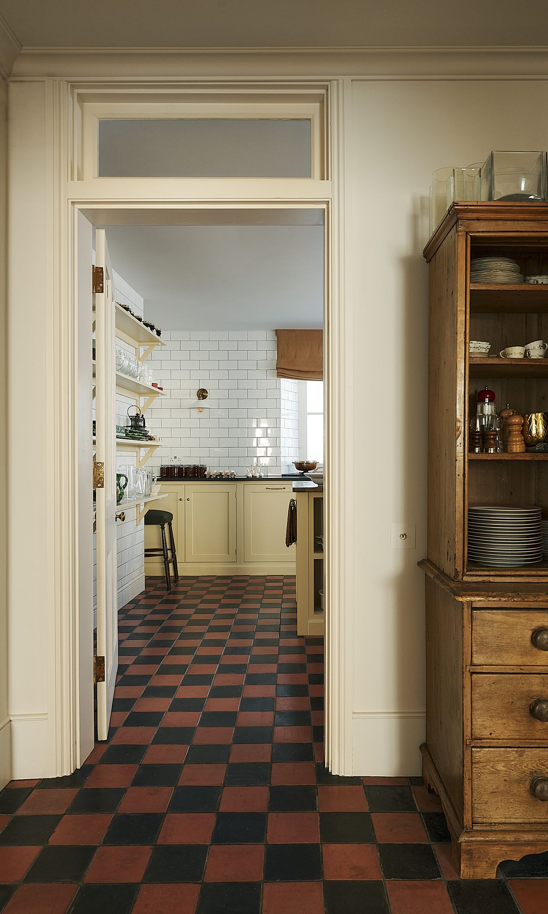 Cocina y comedor con vitrina de madera con vajilla, suelo de damero en negro y marrón oscuro