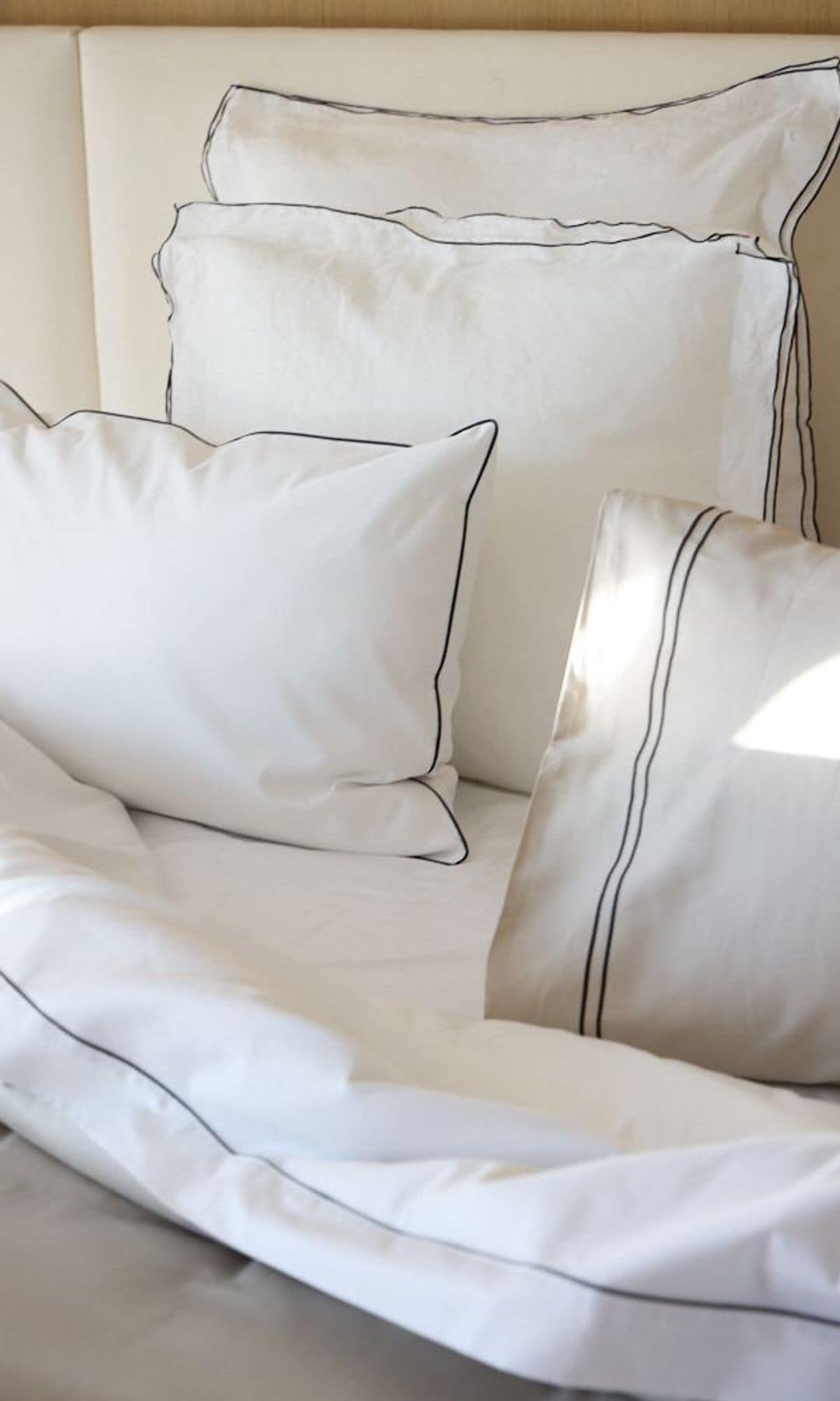 Cama con sábanas blancas, almohadas y cabecero tapizado 