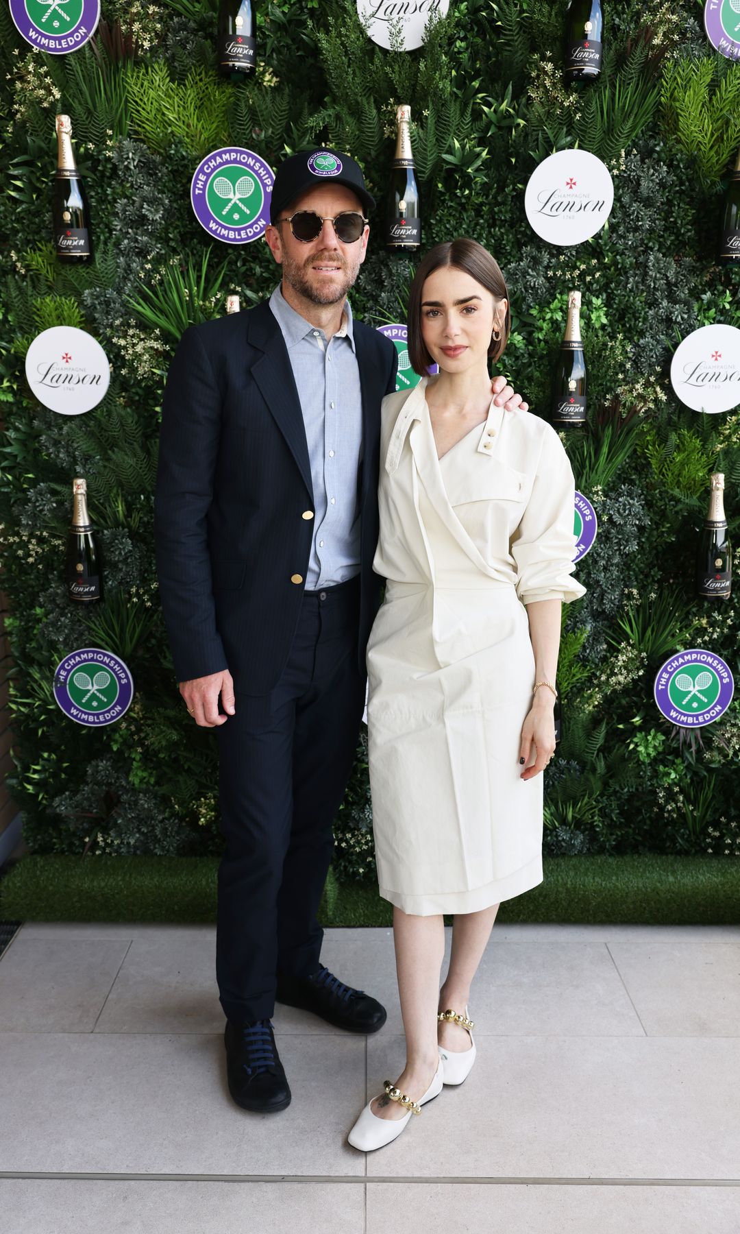 Charlie McDowell y Lily Collins en Wimbledon 2025, ella luciendo un vestido camisero en color blanco (acorde con el torneo) y unas bailarinas del mismo tono 