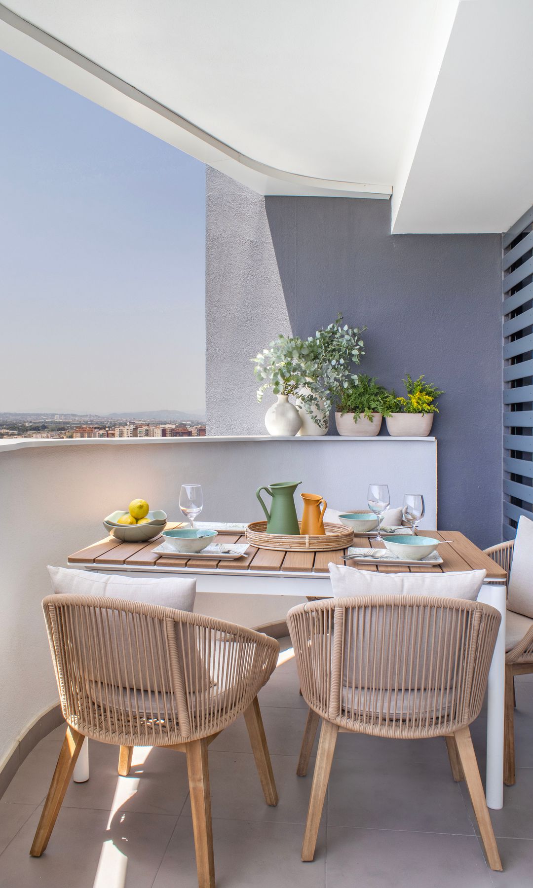Terraza con comedor con mesa de madera, barandilla blanca, jarrones, sillas de fibras vegetales